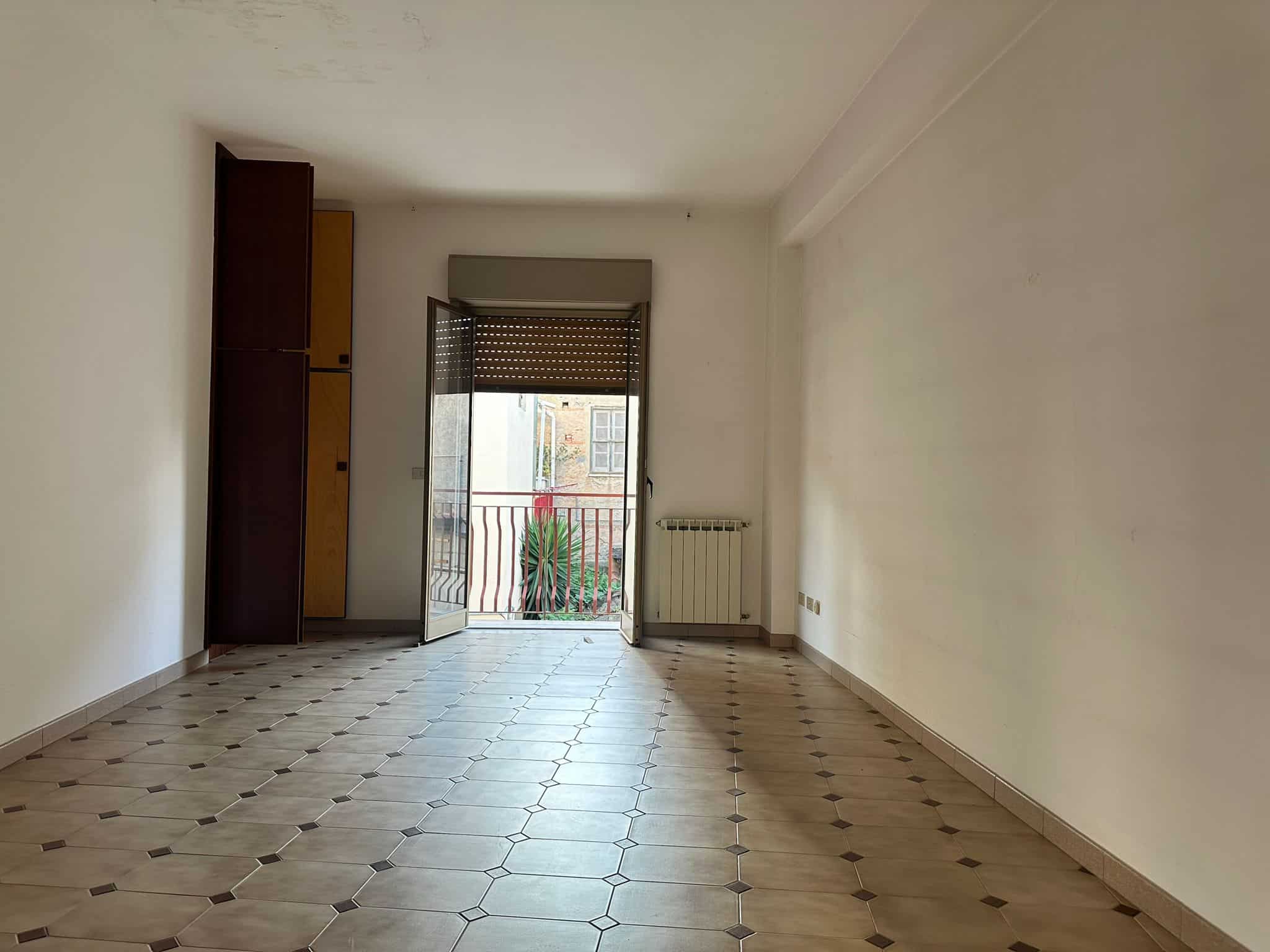 Spazio vuoto e luminoso in appartamento con balcone, pavimento in piastrelle e pareti bianche, ideale per arredamento moderno e personalizzato.