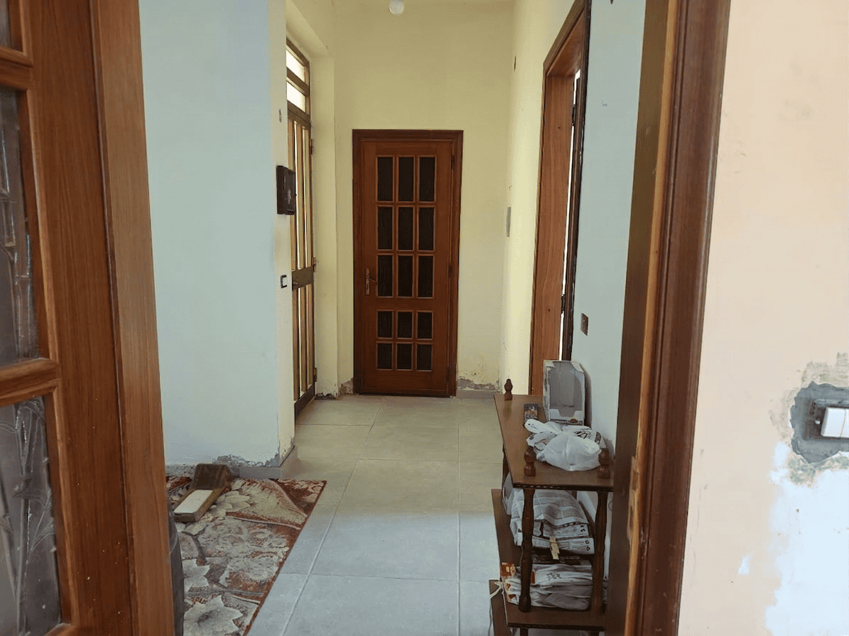 Corridoio interno di una casa con porta in legno e pareti in fase di ristrutturazione, ambiente luminoso e accogliente.