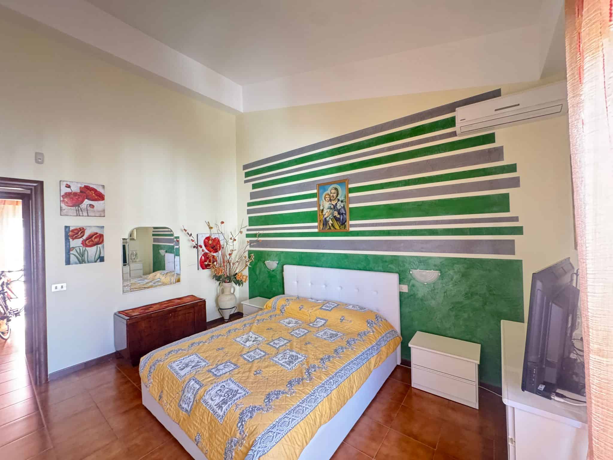 Camera da letto moderna con pareti decorative verdi e gialle, letto matrimoniale e arredi eleganti, ambiente accogliente e luminoso.
