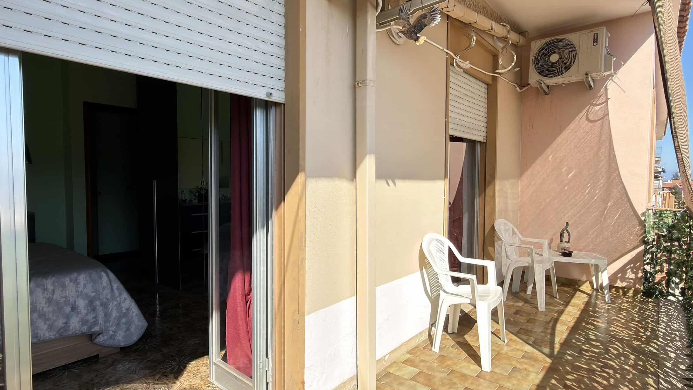Balcone di un appartamento con sedie bianche e aria condizionata, vista luminosa e spazio esterno per relax e svago.