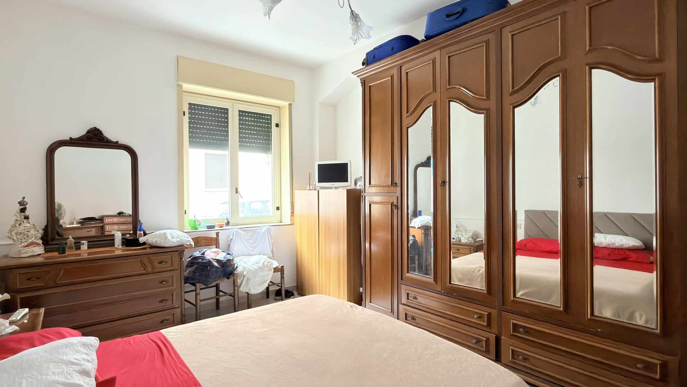 Lavanderia in camera con armadio in legno, letto matrimoniale e finestra luminosa, ambiente accogliente e ben organizzato.