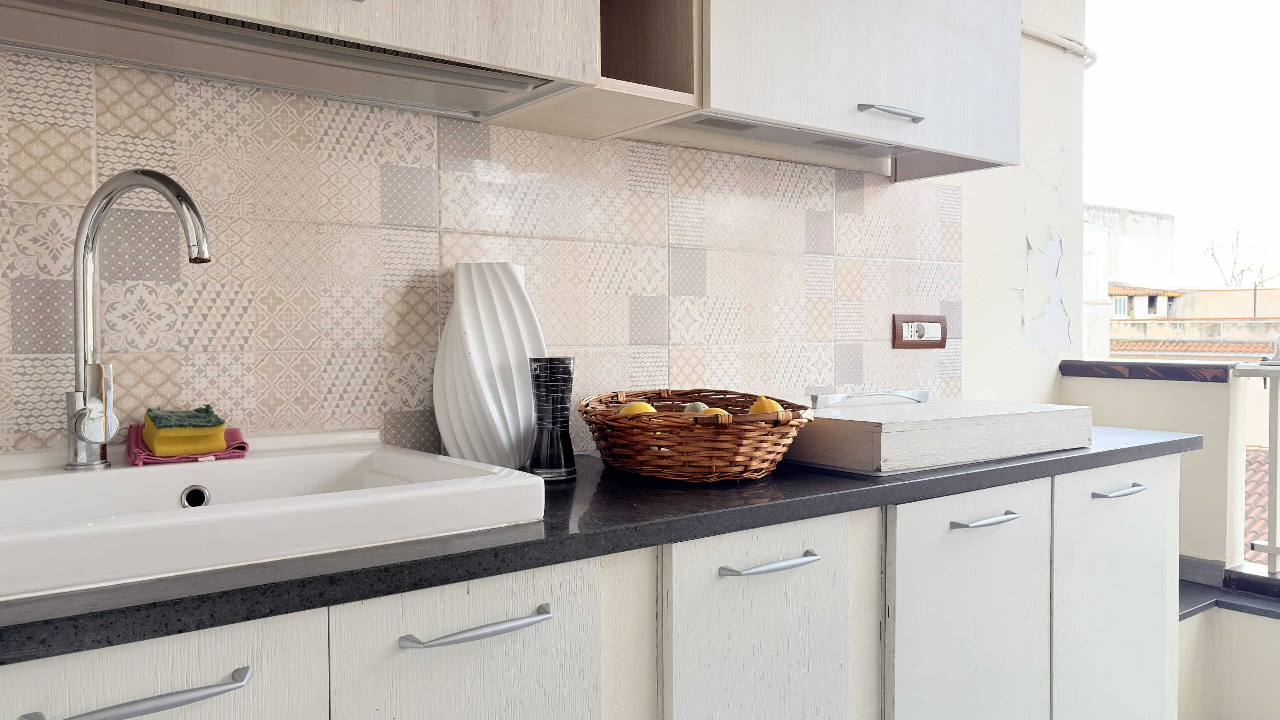 Lavandino da cucina con piano di lavoro nero, accessori eleganti e decorativi, in un ambiente luminoso e moderno.