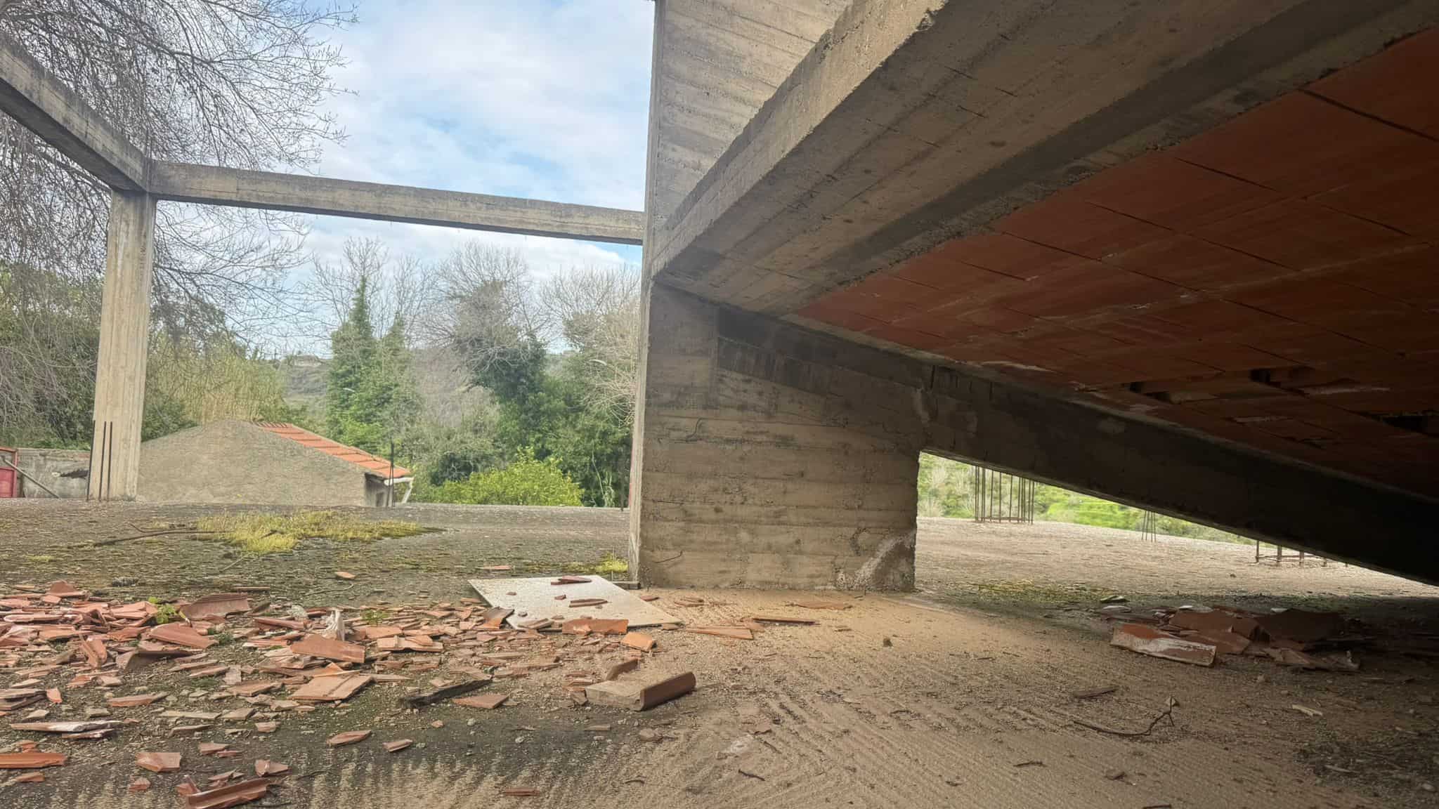 Pavimentazione in cemento e mattoni sotto un ponte in costruzione, con elementi di edilizia e ambiente esterno naturale.