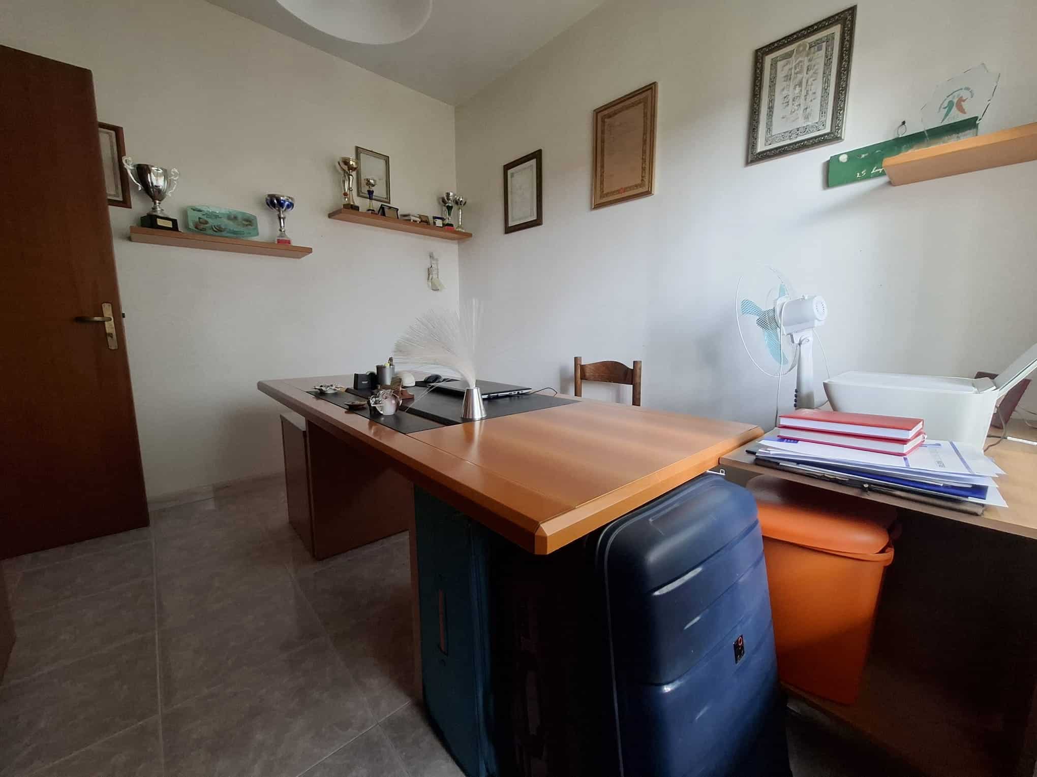 Una stanza da ufficio con scrivania, sedia e scaffali con trofei e documenti, ambiente luminoso e ordinato, ideale per lavoro o studio.