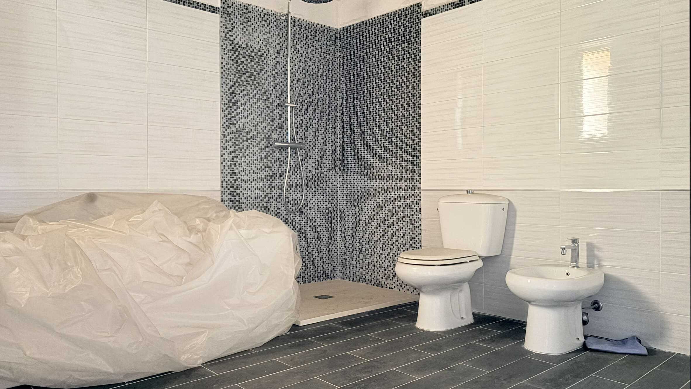 Acqua calda e doccia nel bagno moderno con piastrelle bianche e parete a mosaico blu scuro, con sanitari bianchi e pavimento in piastrelle grigie.