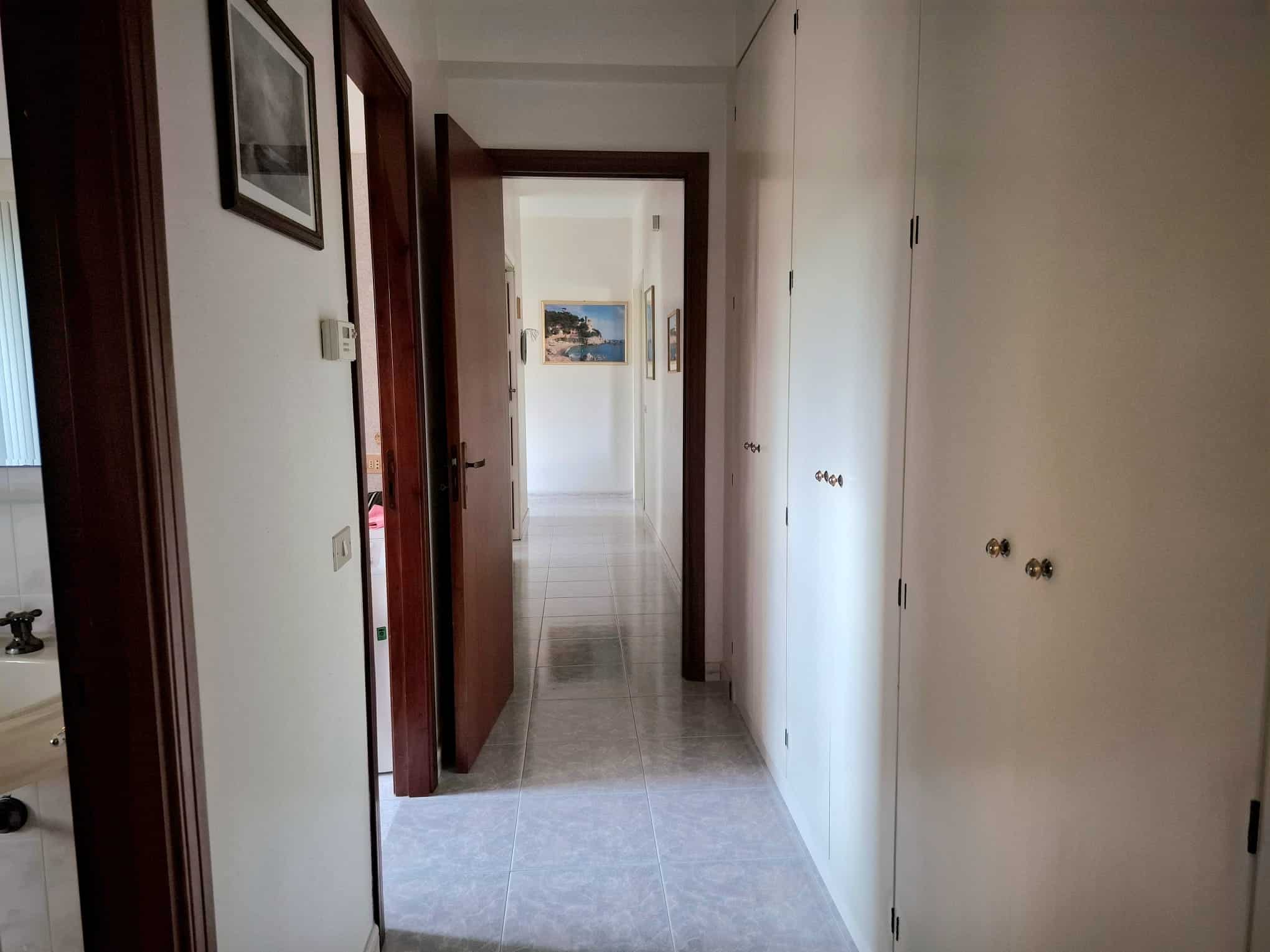 Ampio corridoio interno di una casa con pareti bianche, porte in legno e armadiature a muro, ambiente luminoso e ben organizzato.