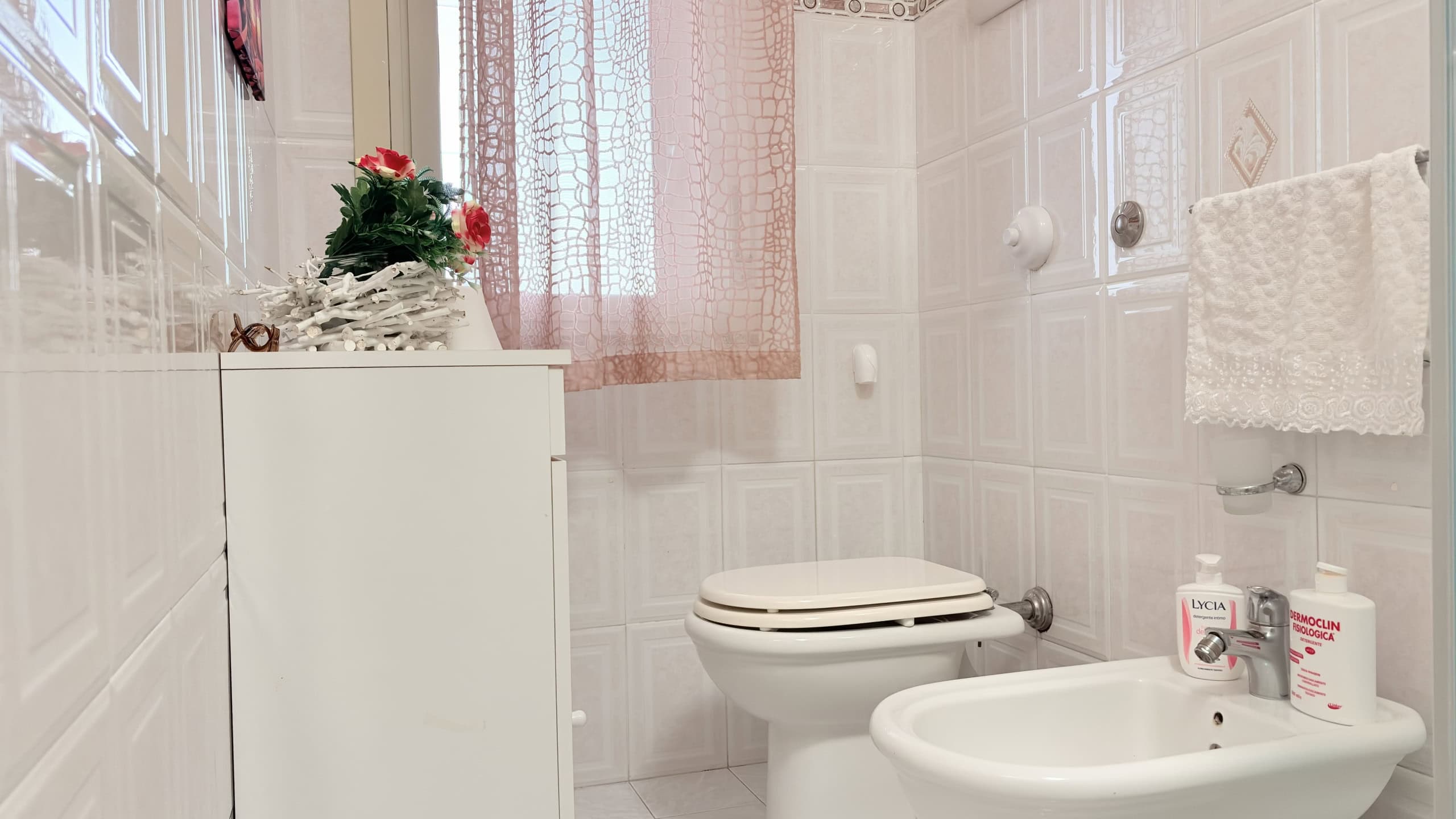 Piantina di un bagno moderno con sanitari bianchi, asciugamano e decorazioni floreali, ideale per case in vendita o affitto.