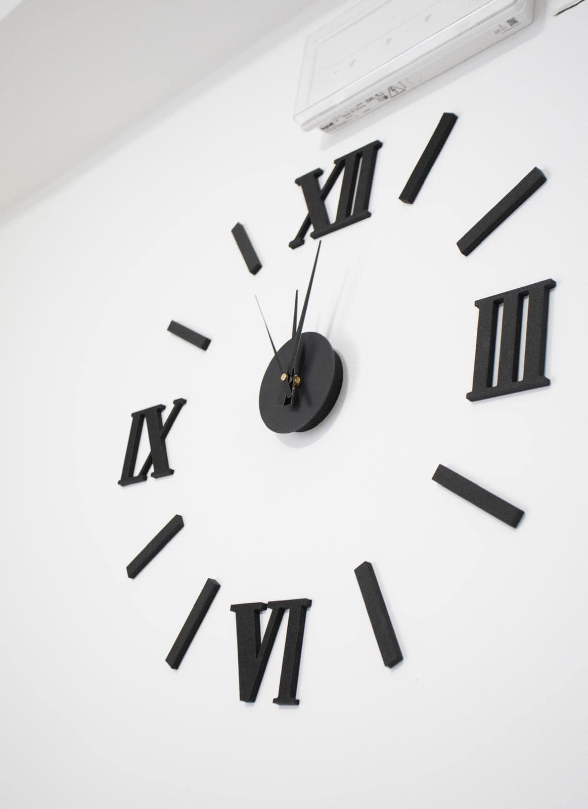 Aggiunta di un grande orologio da parete moderno con numeri romani neri su una parete bianca, ideale per arredare ambienti eleganti e minimalisti. Perfetto per case e uffici contemporanei.