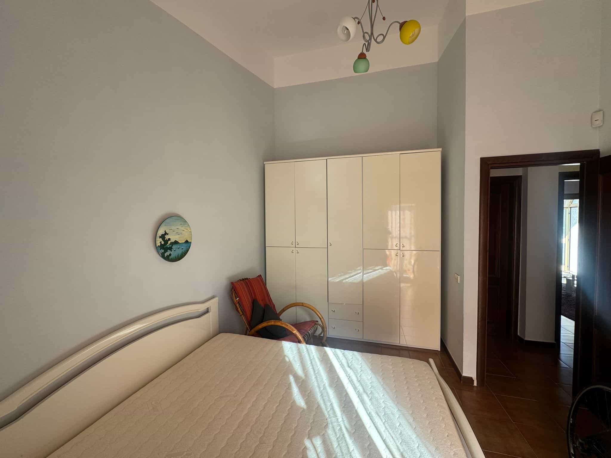 Il letto matrimoniale in una camera moderna con pareti chiare, armadio a muro e sedie, illuminata dalla luce naturale, ideale per soggiorni confortevoli e rilassanti.