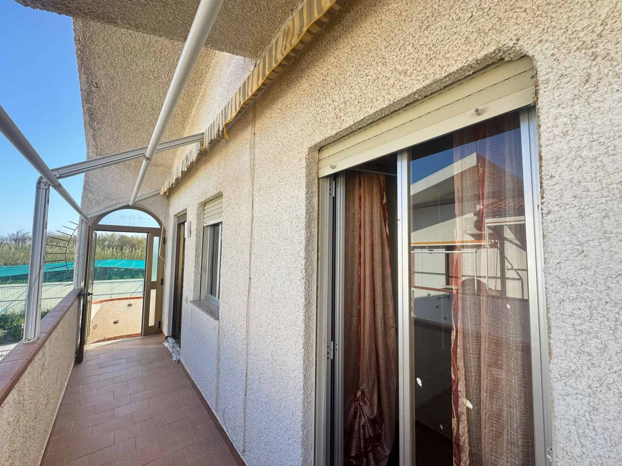 Balcone di un appartamento con vista panoramica, struttura in muratura e infissi in vetro con tende di tessuto, ambiente luminoso e spazioso ideale per relax e svago all'aperto.
