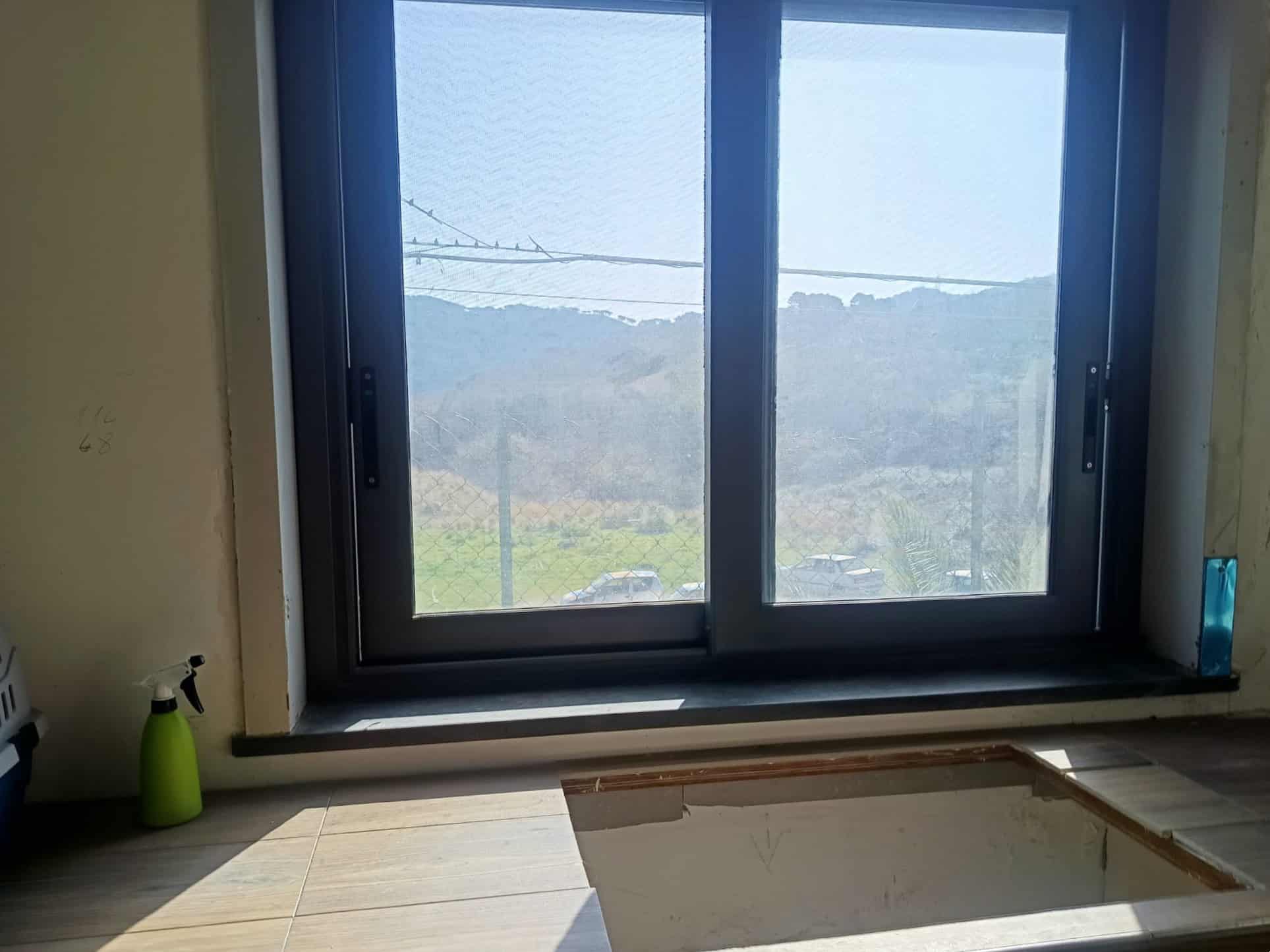 Vista panoramica attraverso una finestra moderna con doppio vetro, che mostra un paesaggio naturale con colline e cielo sereno, ideale per ambienti residenziali e immobili di pregio.