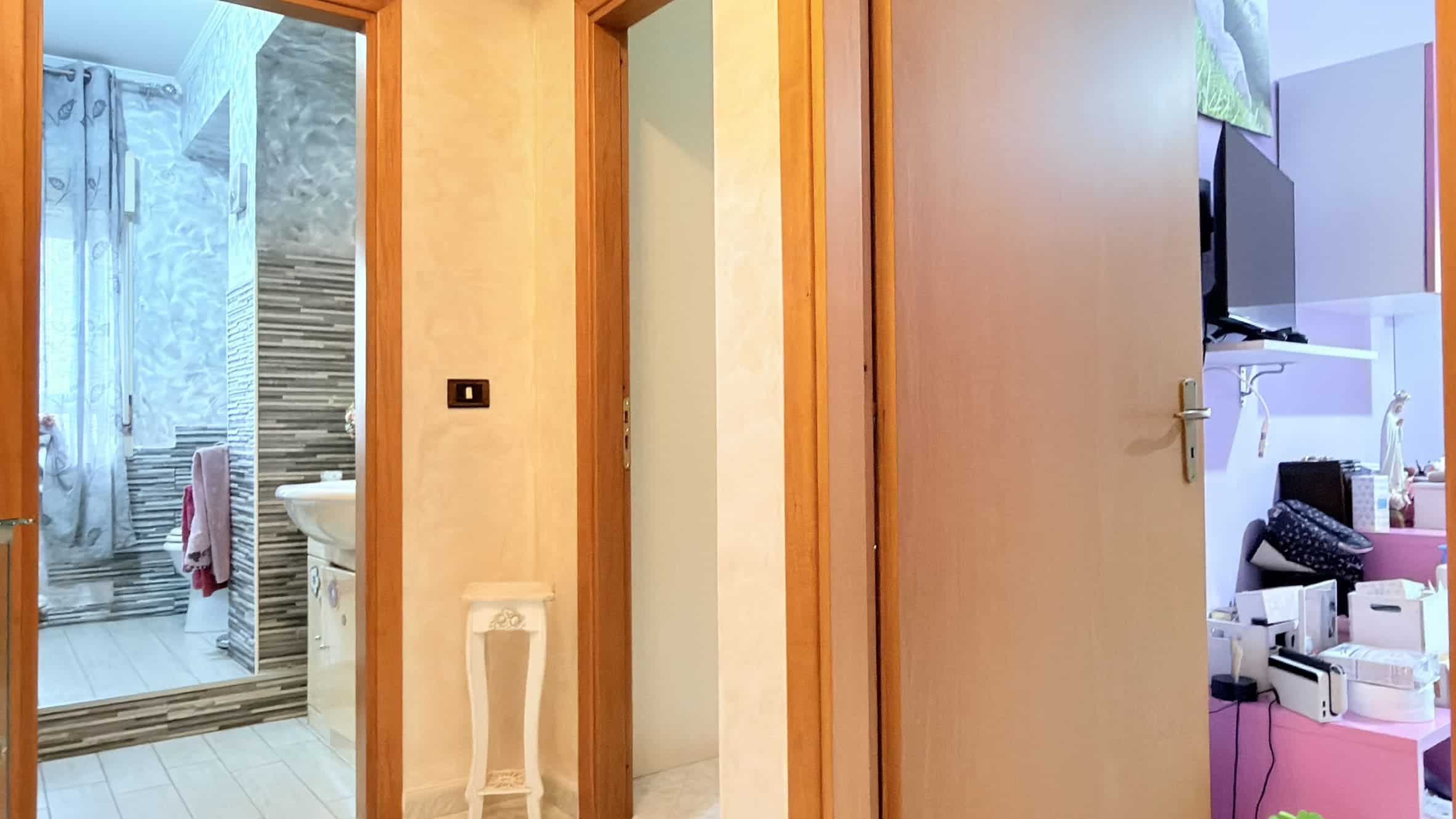 Spogliatoio e bagno con doccia in una casa moderna, vista attraverso una porta aperta, con dettagli di arredo funzionali e colori neutri, ideale per ambienti di comfort e praticità.