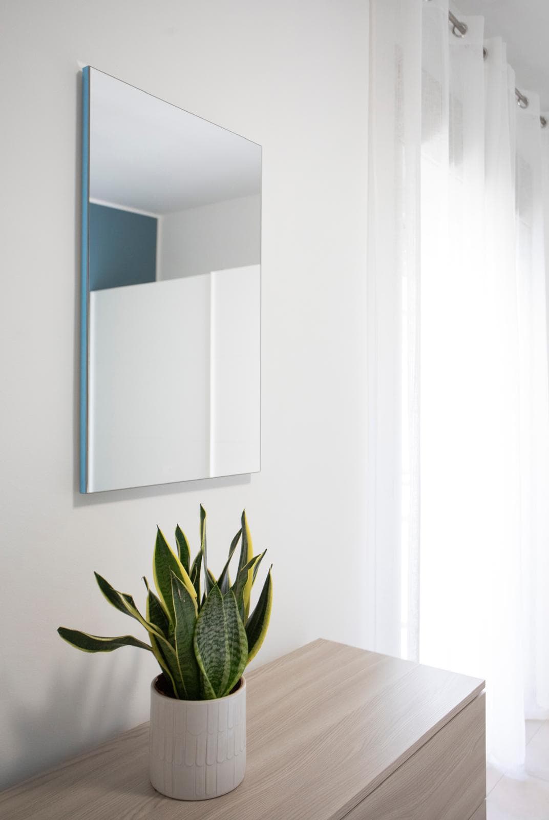 Specchio moderno con pianta decorativa in un ambiente luminoso e minimalista, ideale per arredi eleganti e funzionali. Perfetto per valorizzare l’ingresso o il soggiorno.