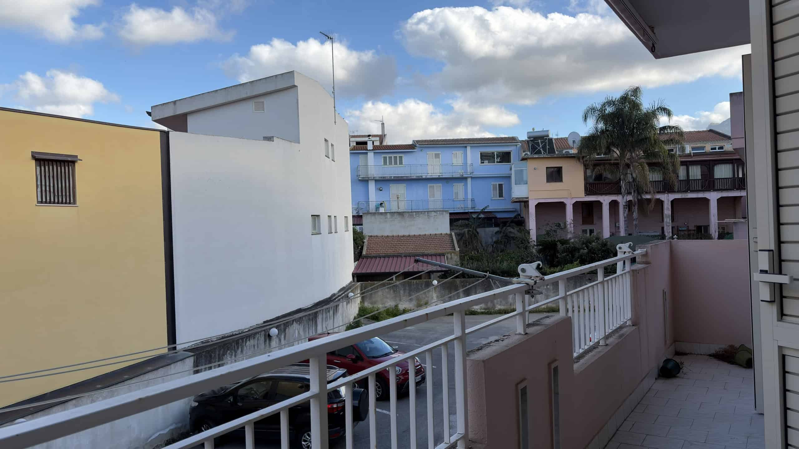 Balcone con vista su edifici residenziali in un quartiere urbano, cielo sereno con nuvole bianche, ambiente luminoso e tranquillo, ideale per relax e momenti di svago all'aperto.