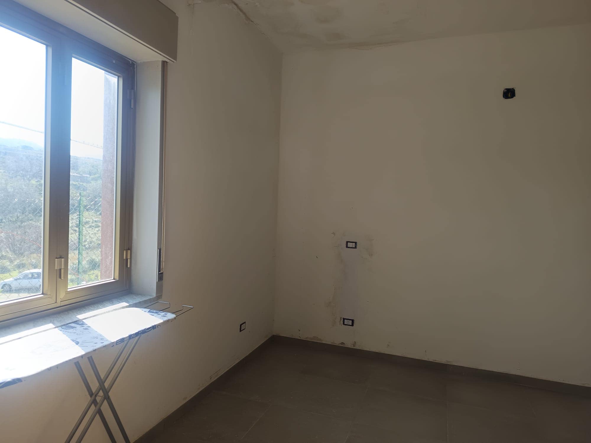Pannello di finestra in una stanza vuota in fase di ristrutturazione, con pareti bianche e pavimento in piastrelle grigie, pronta per essere personalizzata.