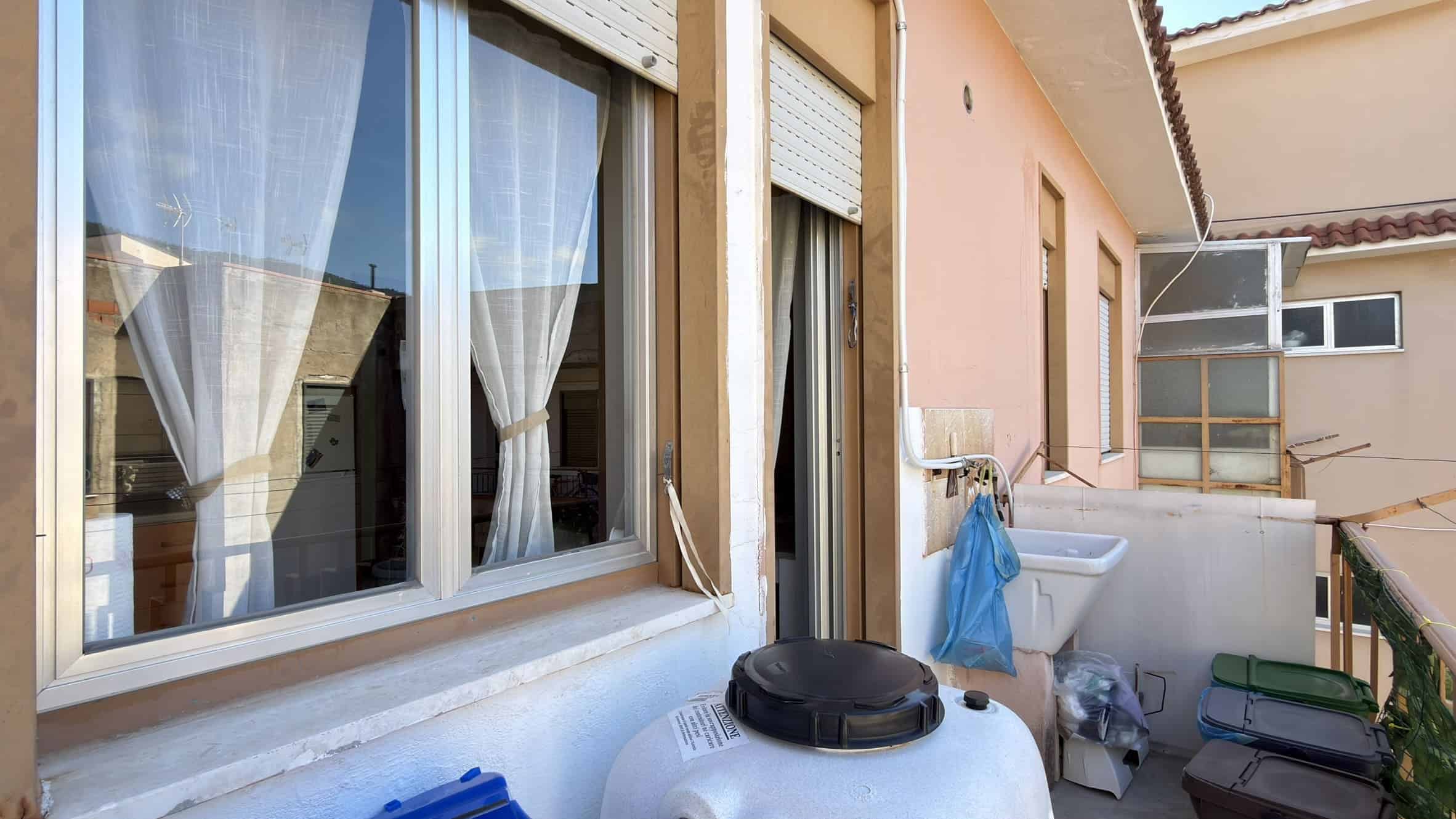 Lavatrice esterna e spazio lavanderia in un balcone di un appartamento, con vista su edifici vicini, ambiente pratico e funzionale per le faccende domestiche all'aperto.