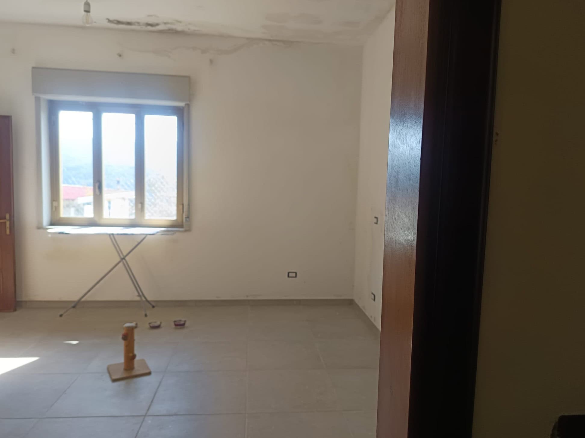 Ampio soggiorno vuoto con finestra luminosa, pareti bianche e pavimento in piastrelle, pronto per arredamento, in un appartamento in vendita o affitto a NextCasa.