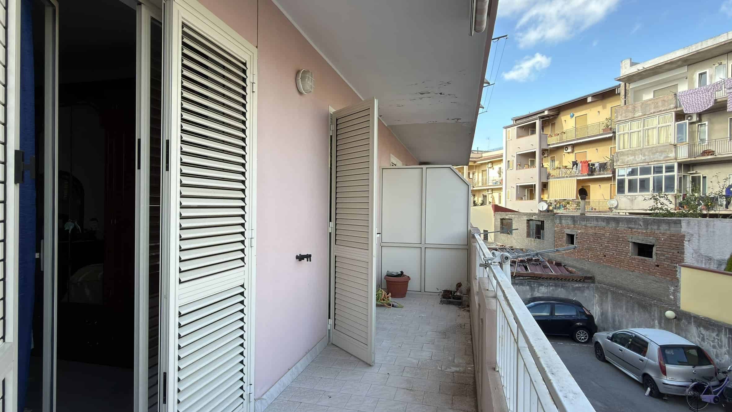 Ampio balcone con vista su strada urbana, con piante e sedie, in un appartamento situato in un quartiere residenziale di città.