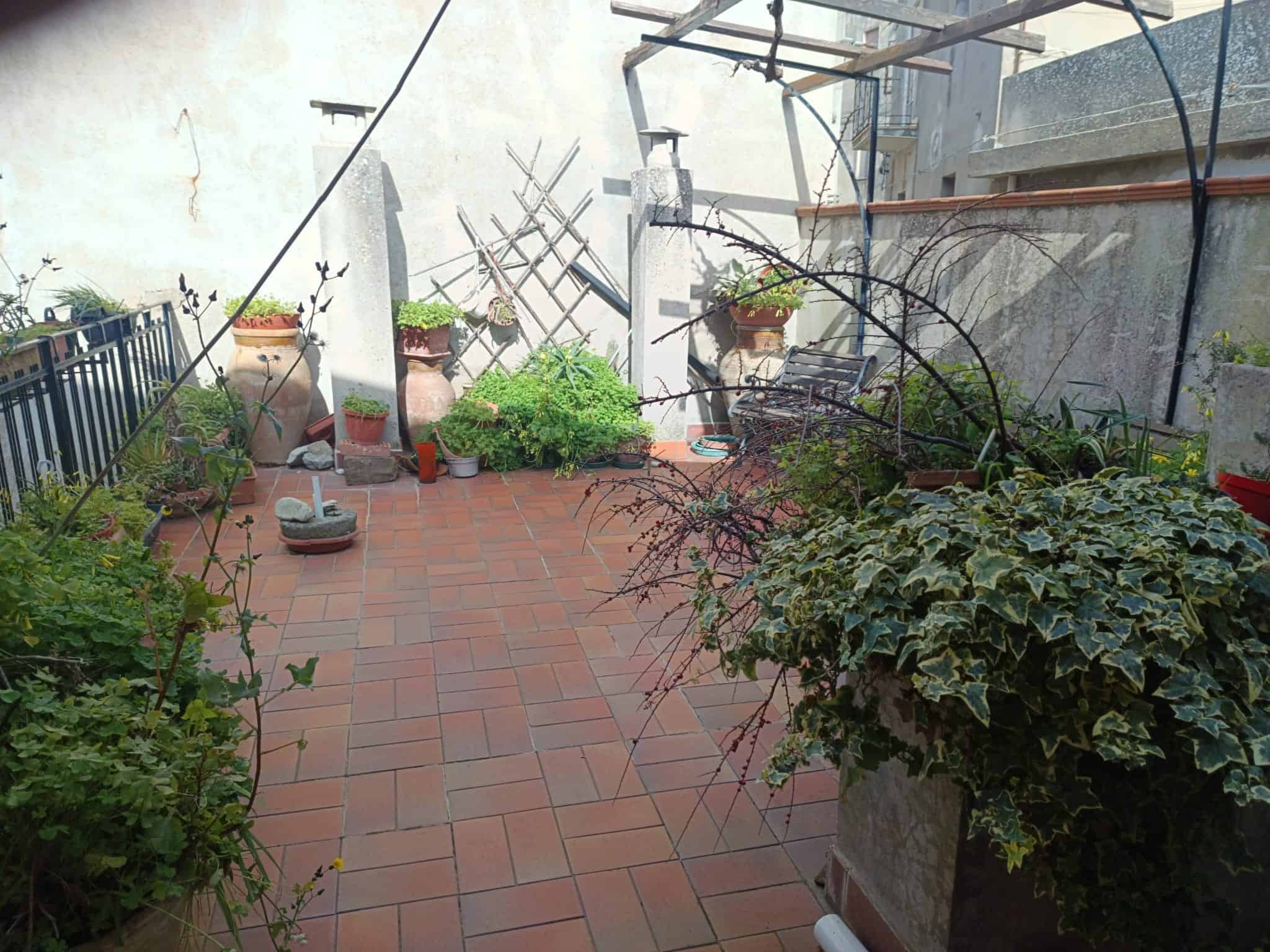 Balcone con piante e fiori, spazio esterno in stile urbano, ideale per relax e coltivazione di piante ornamentali, con pavimentazione in piastrelle di terracotta e decorazioni verdi.