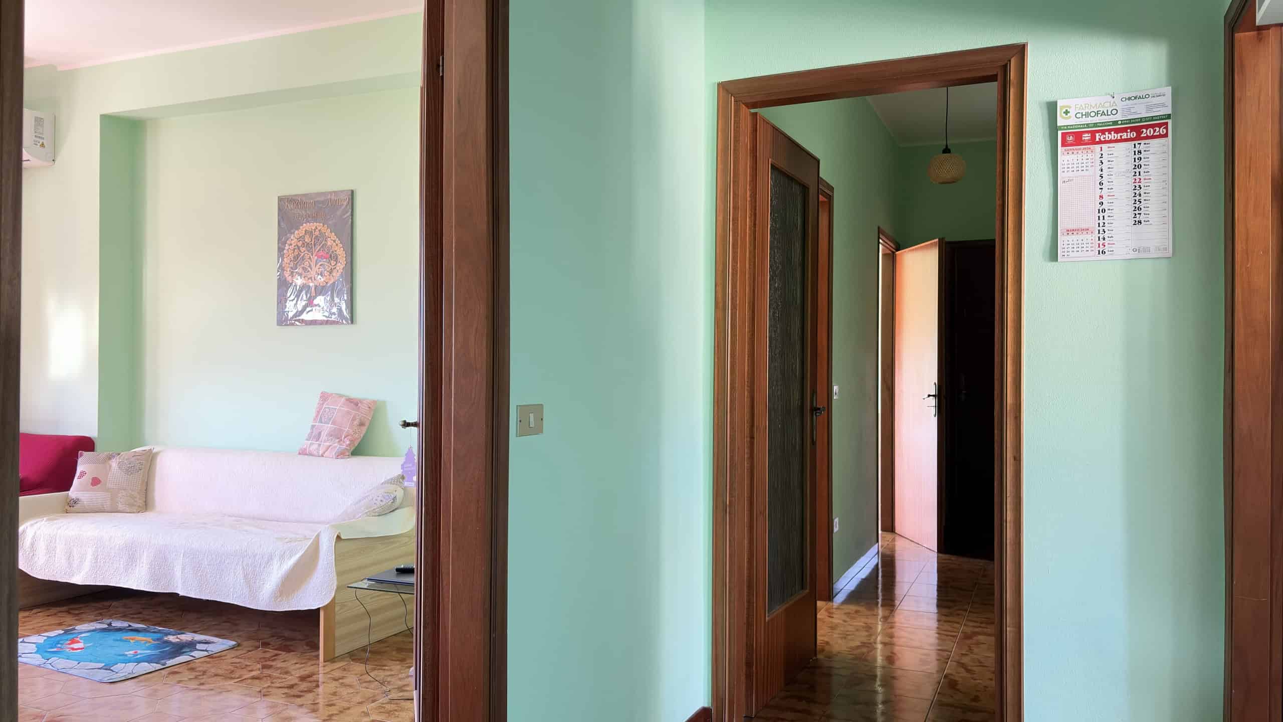 Porta di ingresso in legno con vetro, vista di un corridoio in un appartamento luminoso con pareti verde menta.