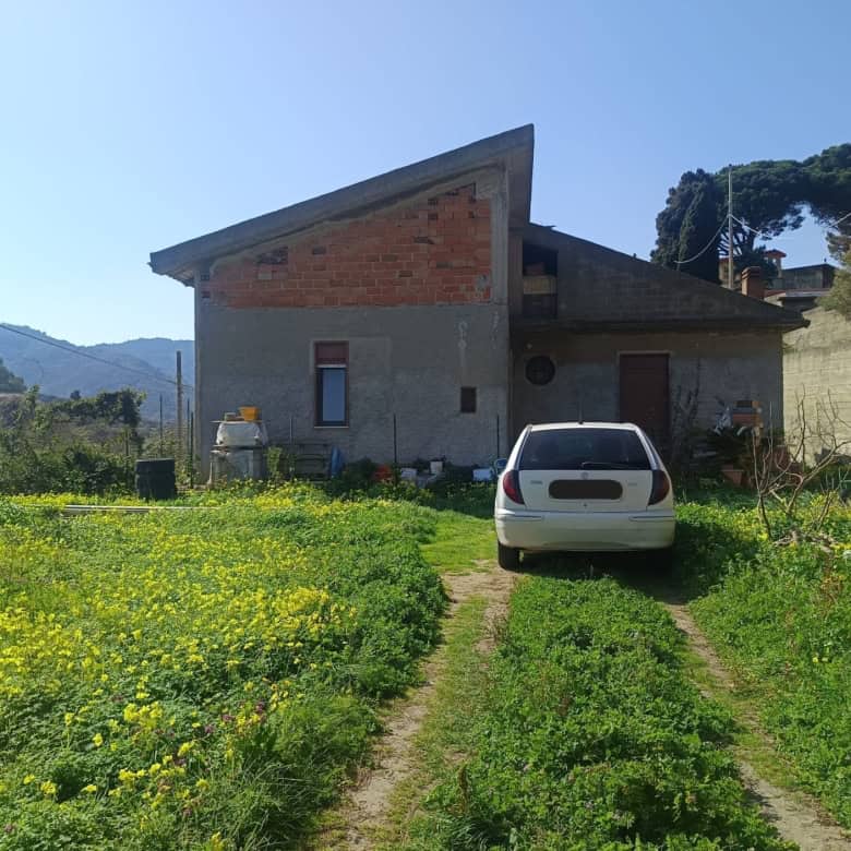 Casa indipendente in campagna con giardino verde e auto parcheggiata, scenario rurale con montagne e cielo sereno, ideale per investimento immobiliare o residenza tranquilla.