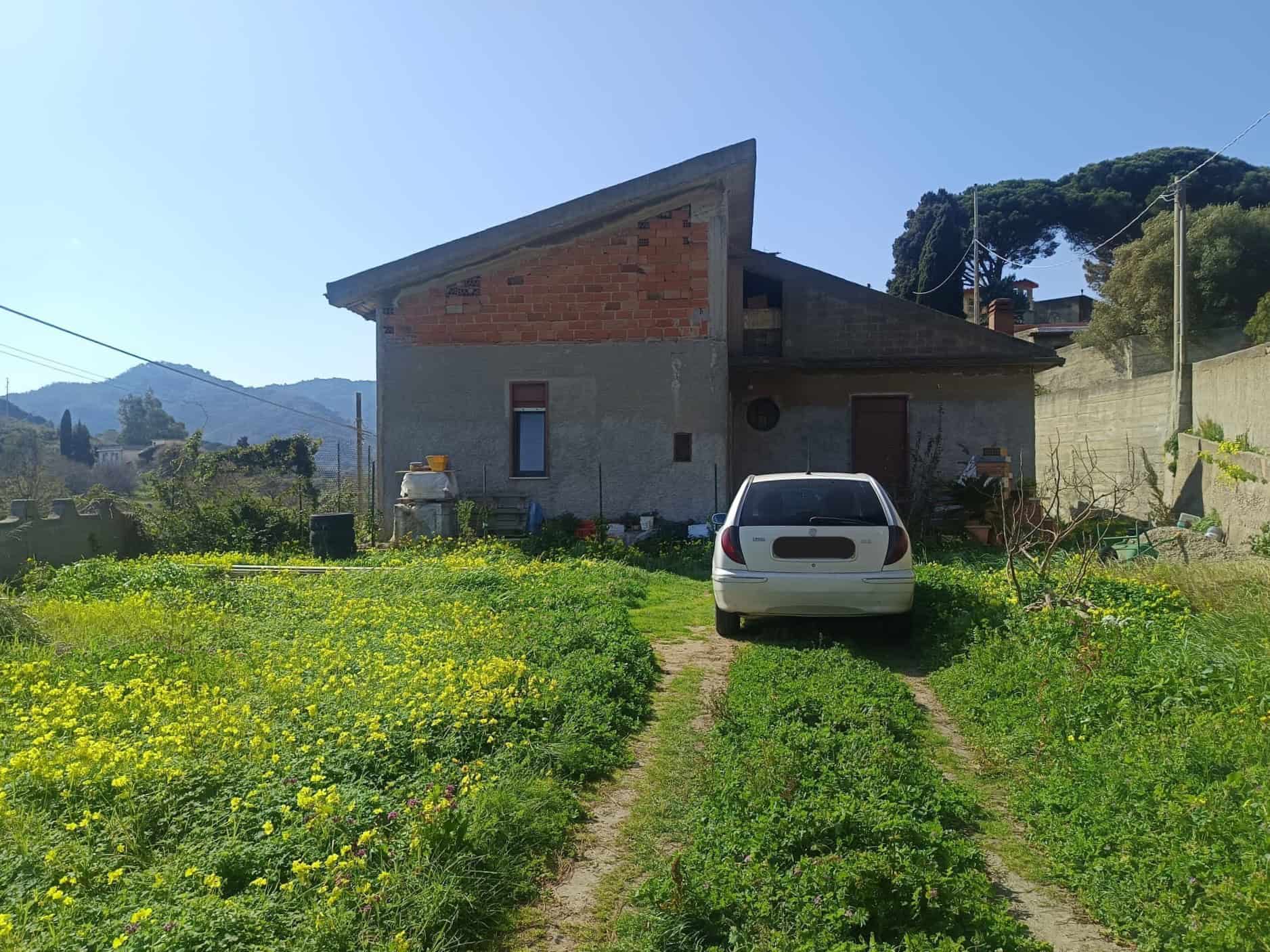 Casa indipendente in campagna con giardino verde e auto parcheggiata, scenario rurale con montagne e cielo sereno, ideale per investimento immobiliare o residenza tranquilla.