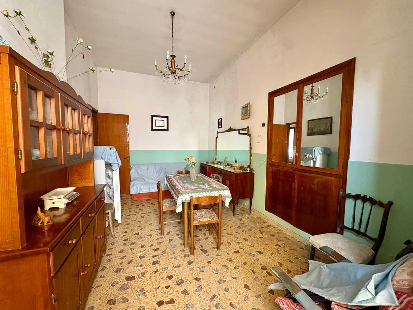 Ottima idea di arredamento vintage in soggiorno con mobili in legno, tavolo con tovaglia floreale e sedie, specchio antico e decorazioni classiche, atmosfera accogliente e tradizionale.