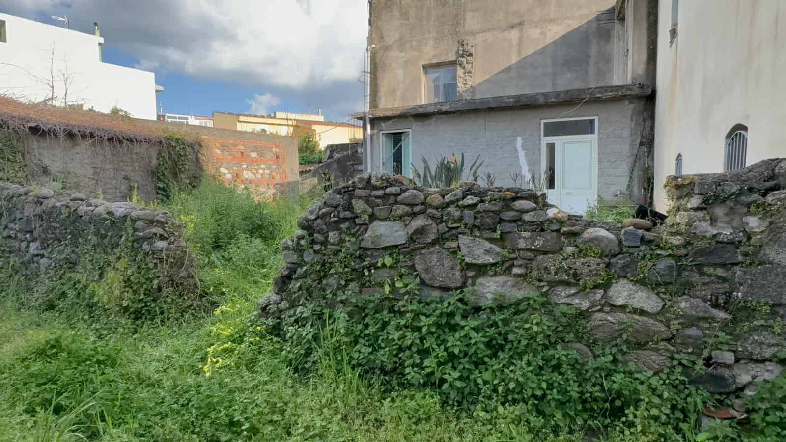 Finestra e parete di un edificio in un contesto urbano con vegetazione e muro di pietra, rappresentando un'area esterna di una proprietà residenziale a NextCasa, specializzata in immobili e soluzioni.