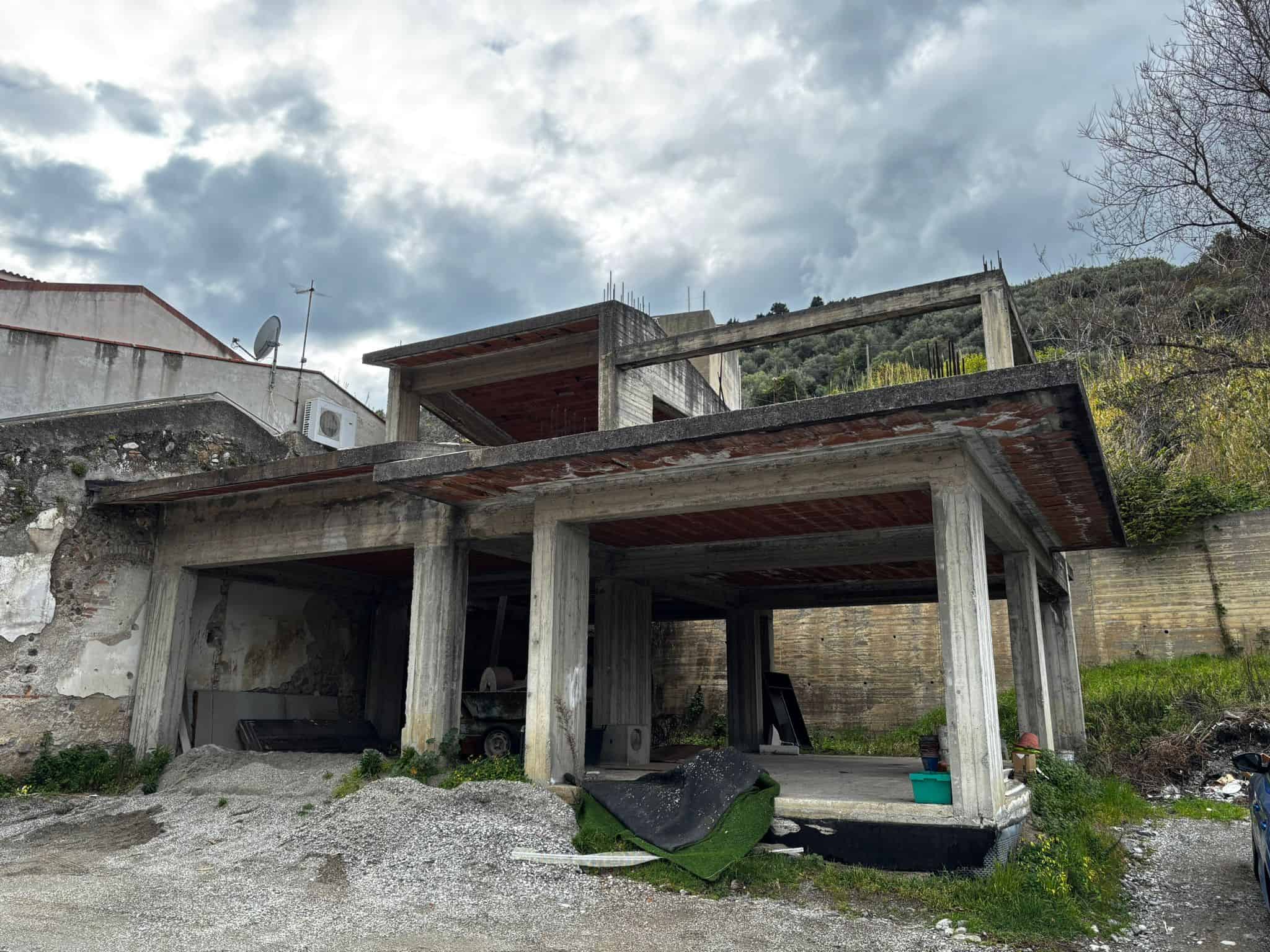 Struttura in cemento di una casa in costruzione con vista sul cielo nuvoloso, in un'area collinare.