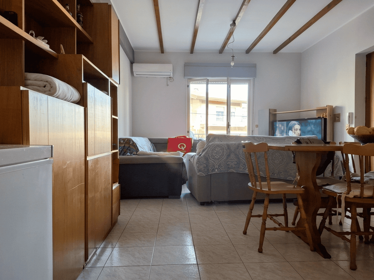 Ampio soggiorno con divani, tavolo in legno e televisore, ambiente luminoso con finestra che lascia entrare luce naturale, arredi moderni e confortevoli, ideale per relax e convivialità.