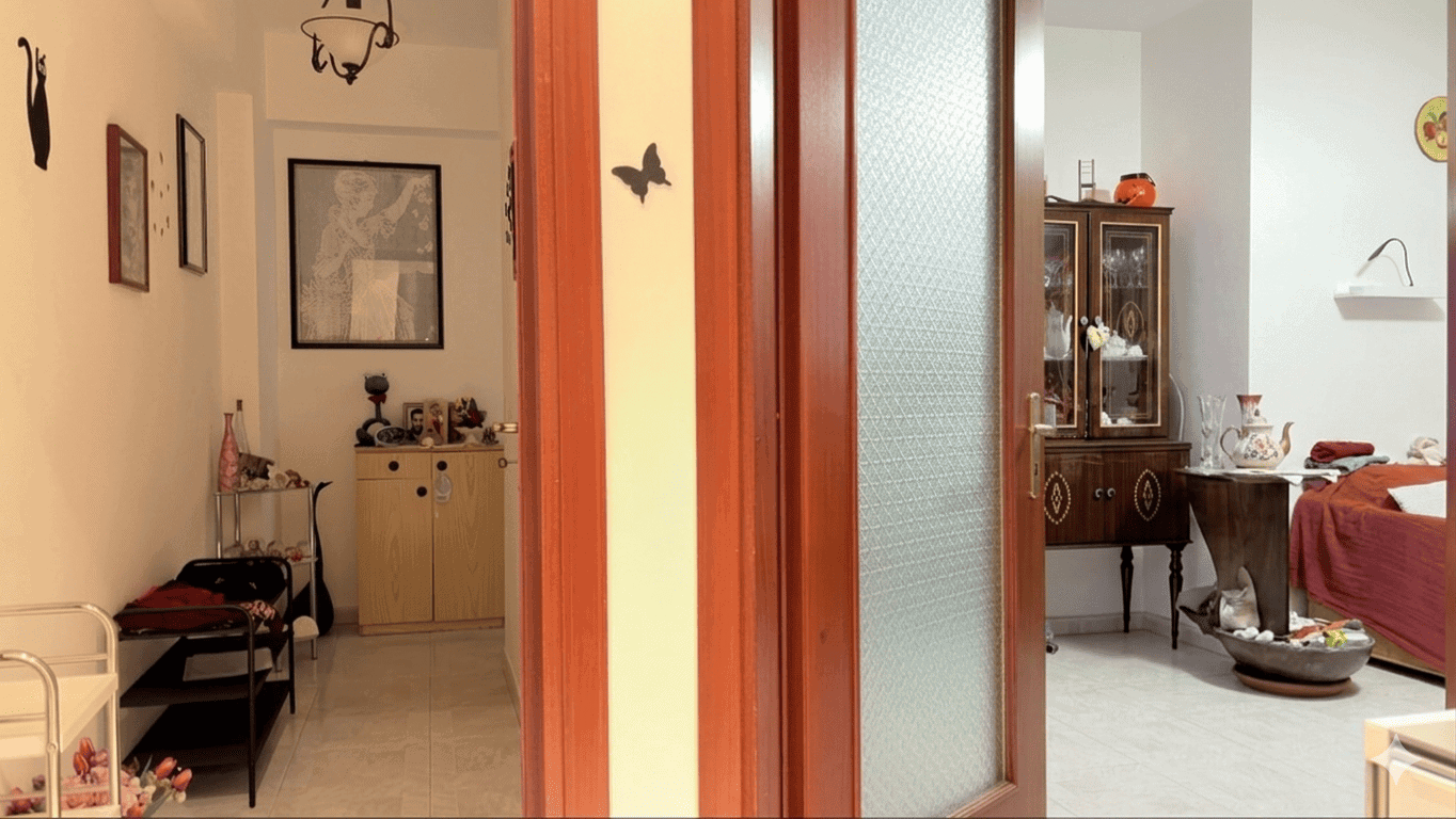 Pannello divisorio tra due ambienti domestici, con porta in vetro e decorazioni murali, in un appartamento arredato con mobili vintage e oggetti decorativi, ideale per soluzioni di design interno.