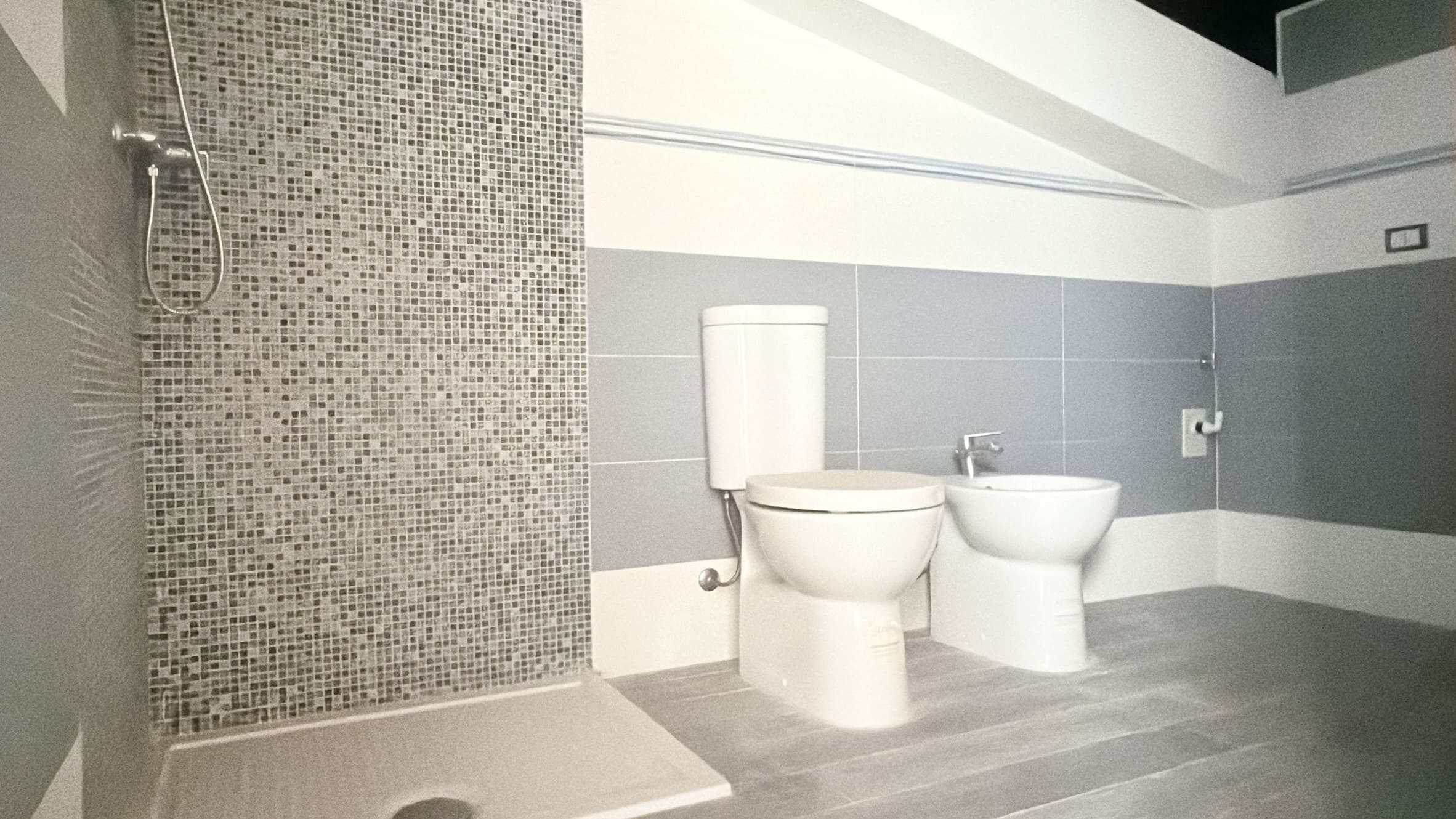 Spazio bagno moderno con WC e bidet, pareti grigie e pavimento in laminato, dettagli di design minimalista, ideale per ambienti di comfort e funzionalità.