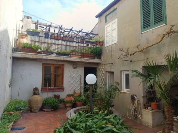 Cortile interno di un appartamento con piante, vasi e arredi, ambiente accogliente e ben curato, ideale per relax e socializzazione, con vista su edifici storici e terrazza superiore.