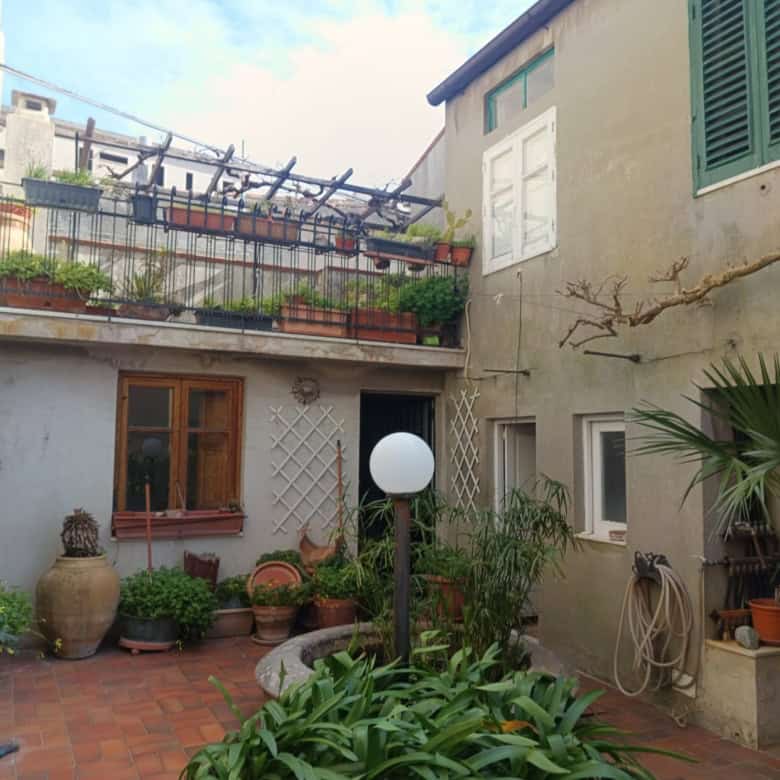 Cortile interno di un appartamento con piante, vasi e arredi, ambiente accogliente e ben curato, ideale per relax e socializzazione, con vista su edifici storici e terrazza superiore.