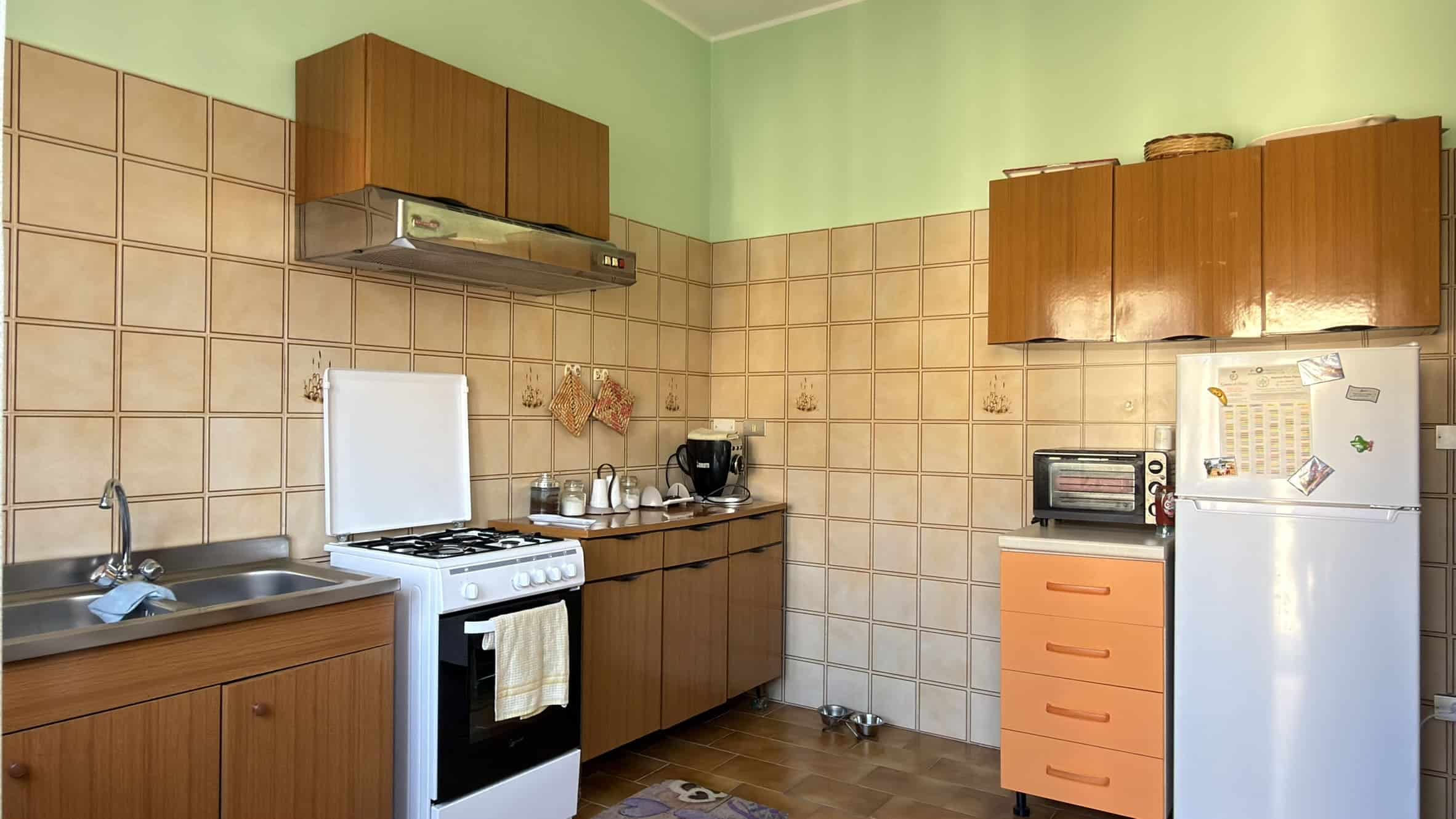 Piatto cucina con mobili in legno, forno, frigorifero e utensili, ambiente domestico funzionale e accogliente.