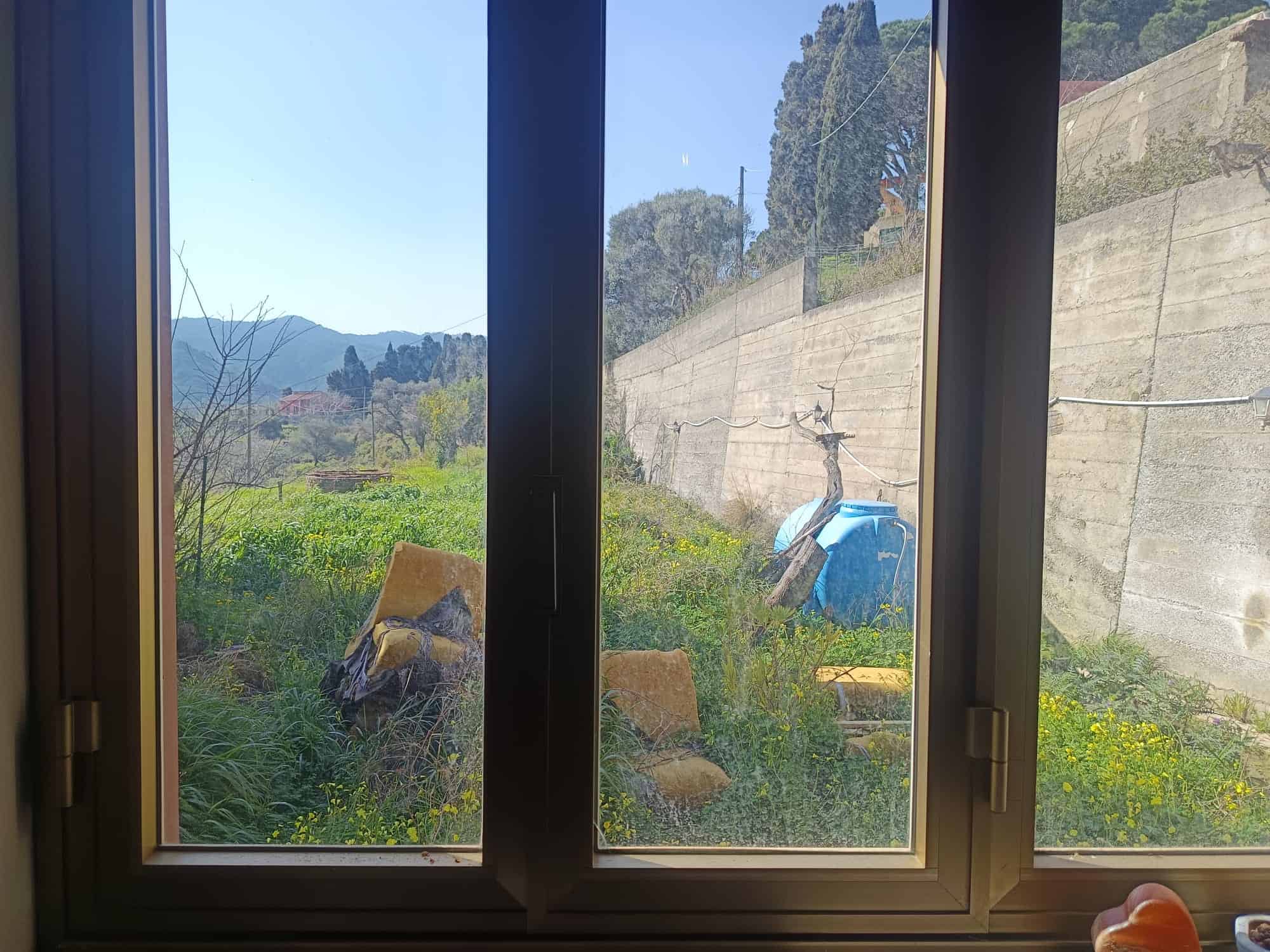 Finestra con vista su giardino verde e paesaggio collinare, ideale per case in campagna o residenze con spazi esterni naturali, in stile moderno e funzionale.