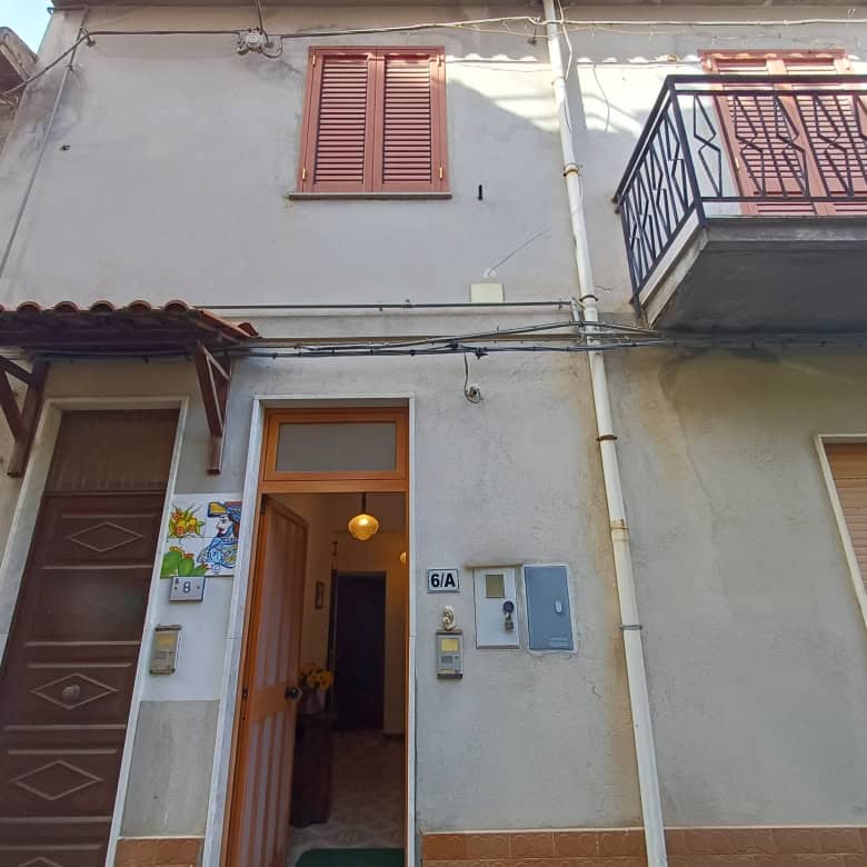 Porte di ingresso e balcone di una casa in stile tradizionale italiano, con finestre con persiane e dettagli architettonici caratteristici, in un contesto urbano residenziale.