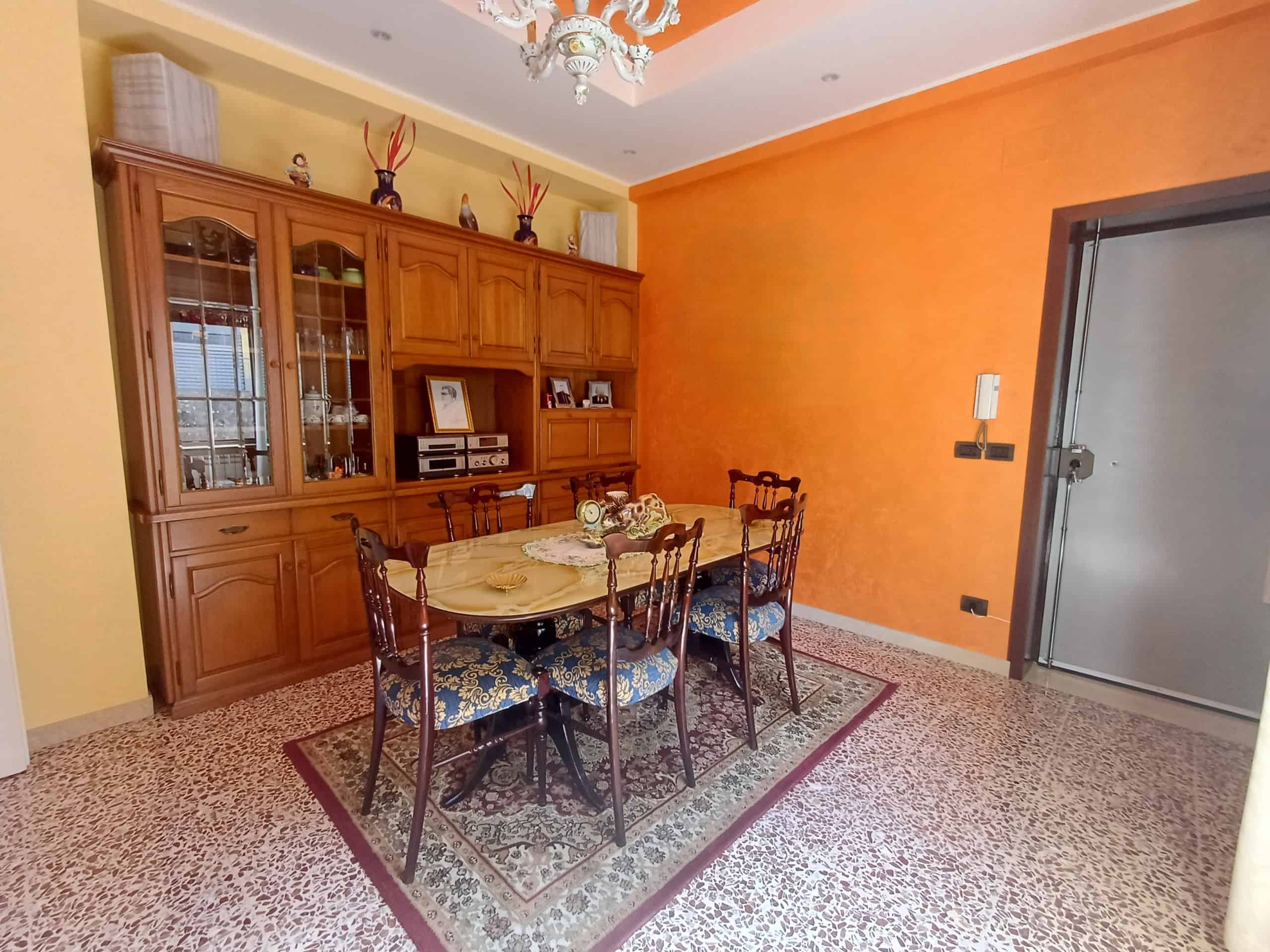Mobili da pranzo eleganti in una sala con pareti arancioni e un grande mobile in legno, ideale per arredamenti di case moderne e accoglienti.