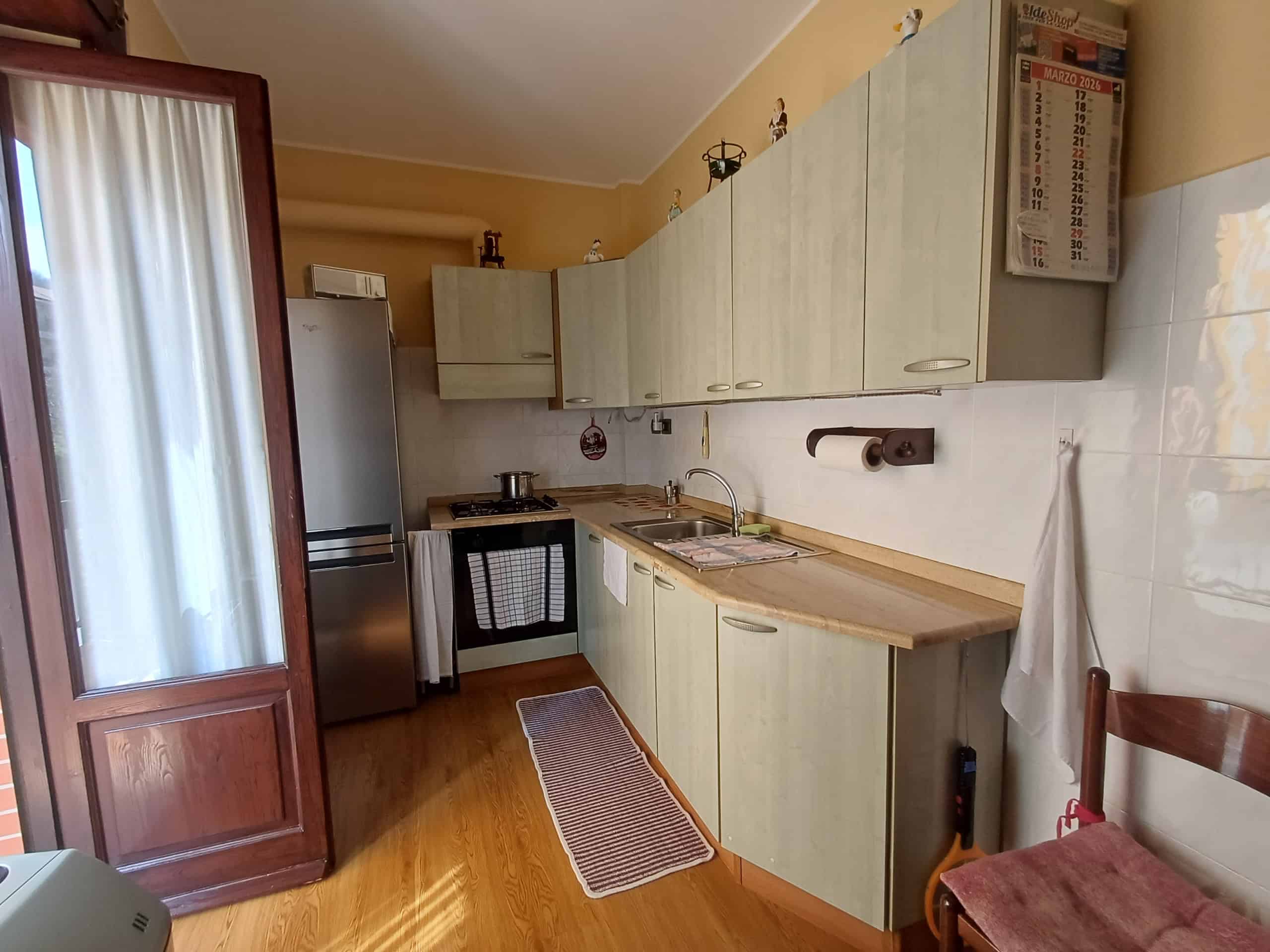 Lavagna di cucina moderna con armadietti chiari, frigorifero e lavello, in un ambiente luminoso e accogliente, ideale per la vita quotidiana.