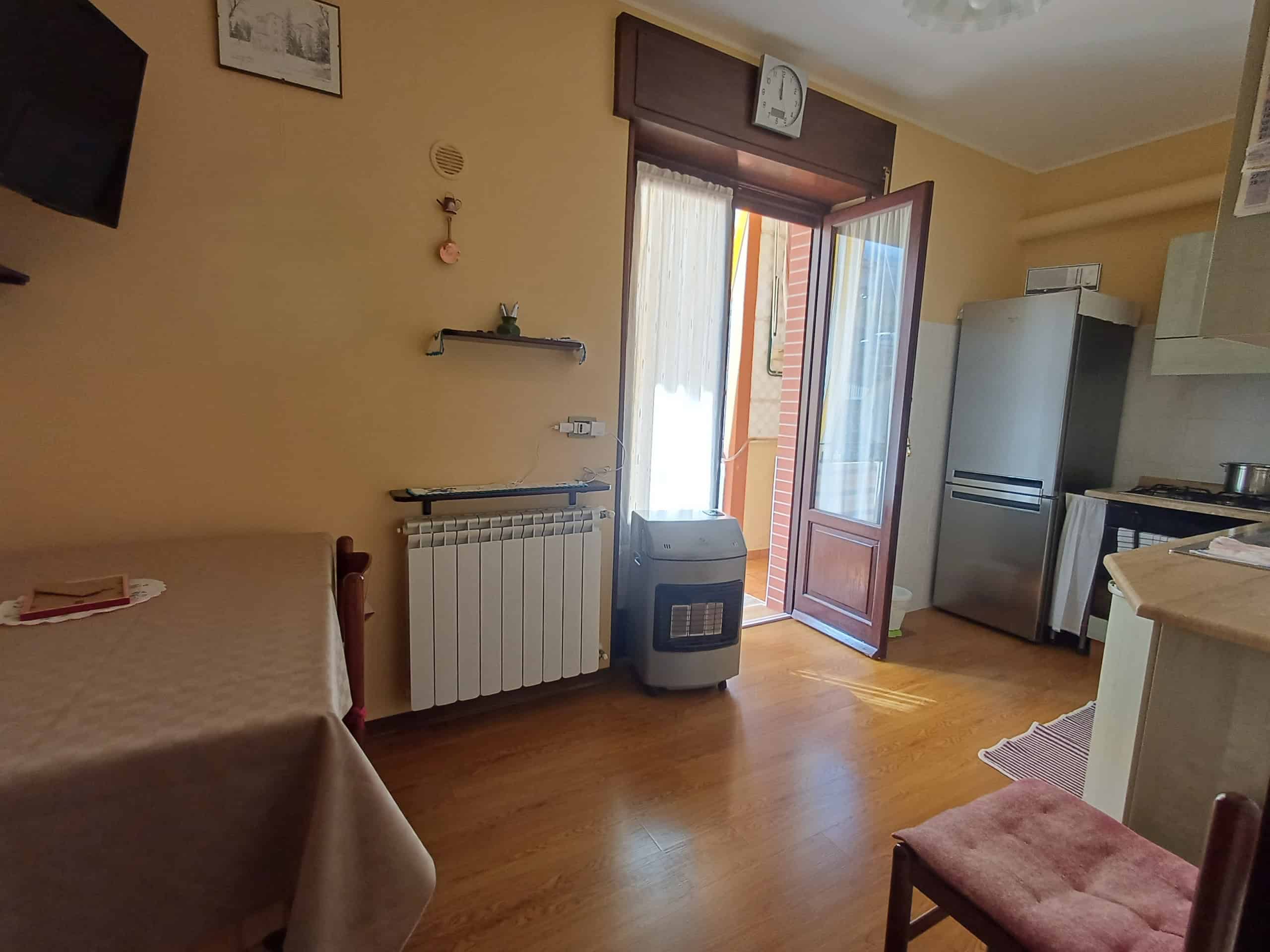 Ampia cucina con balcone, frigorifero, tavolo e sedie, in un appartamento luminoso e accogliente, ideale per soggiorni confortevoli e pratici. Spazio ben organizzato con accesso diretto all'esterno.