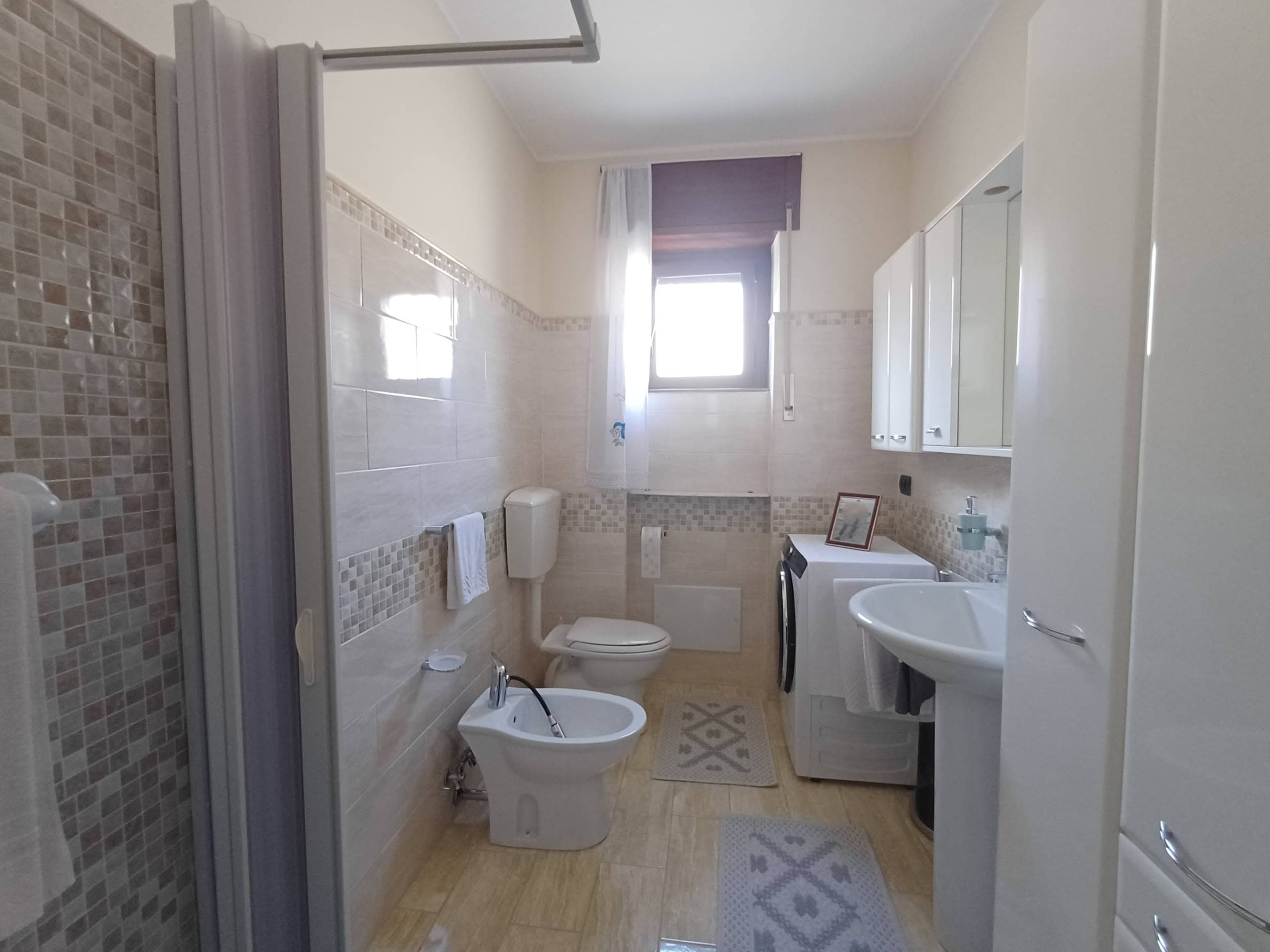 Pulsante doccia e servizi igienici in bagno luminoso con finestra, arredi moderni e sanitari di alta qualità, ideale per comfort e funzionalità.