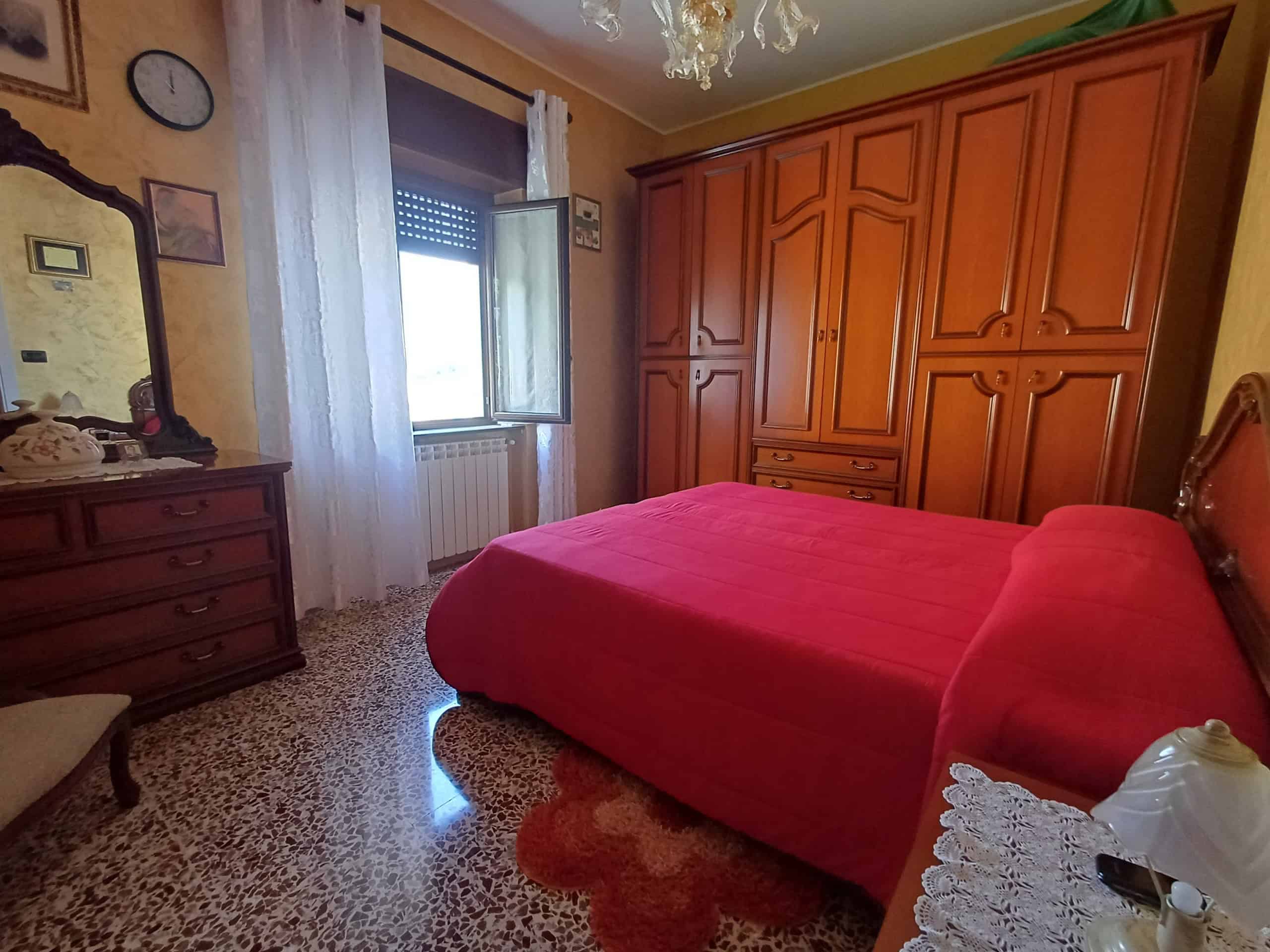 Ampio letto matrimoniale in camera da letto con arredi classici, armadio a muro e comò in legno, illuminata da luce naturale proveniente dalla finestra con tende leggere, in un ambiente accogliente e.