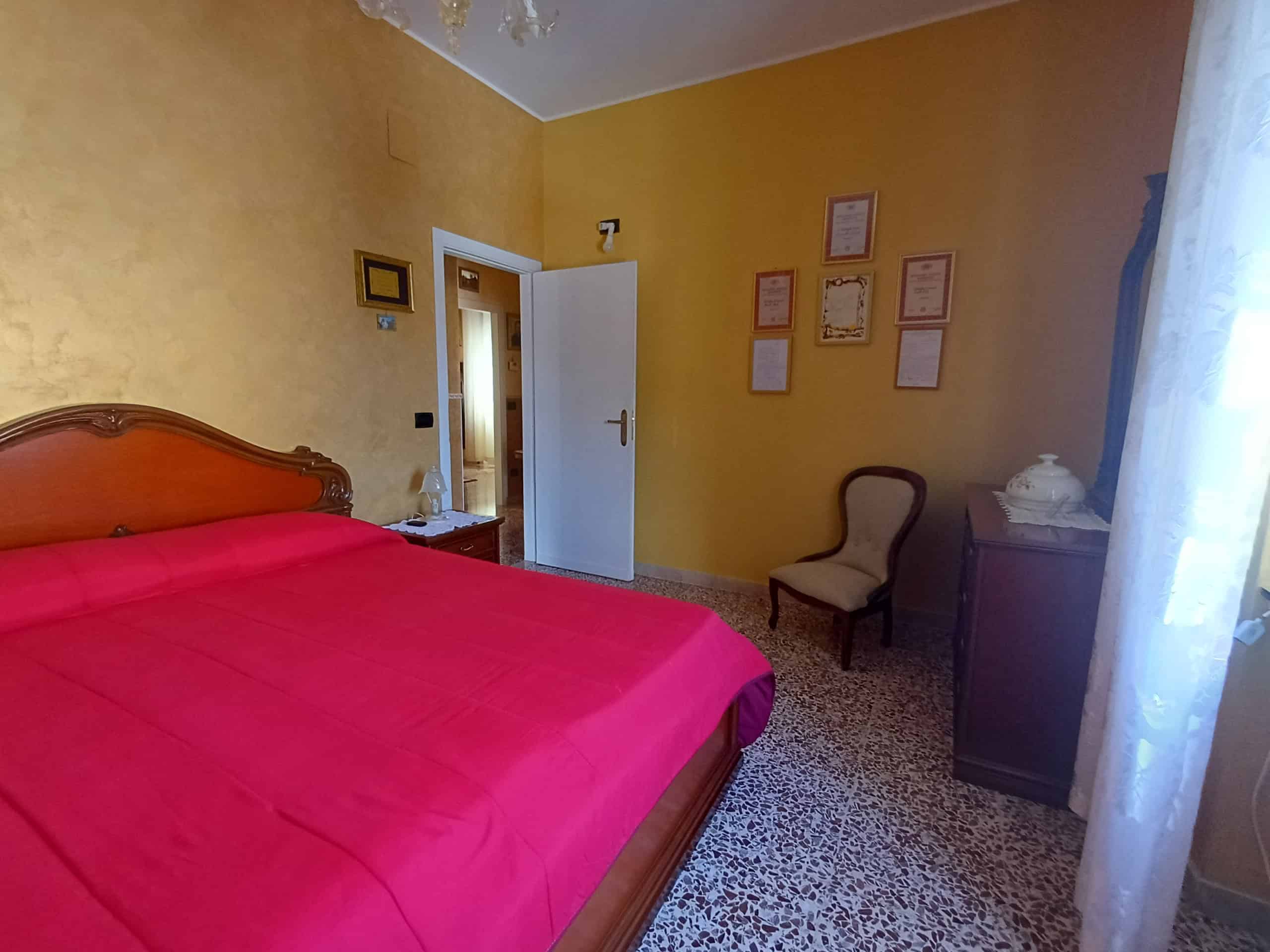Il letto matrimoniale con copriletto rosa in una camera da letto accogliente e ben arredata, con pareti gialle e decorazioni alle pareti, illuminata dalla luce naturale proveniente dalla finestra con.