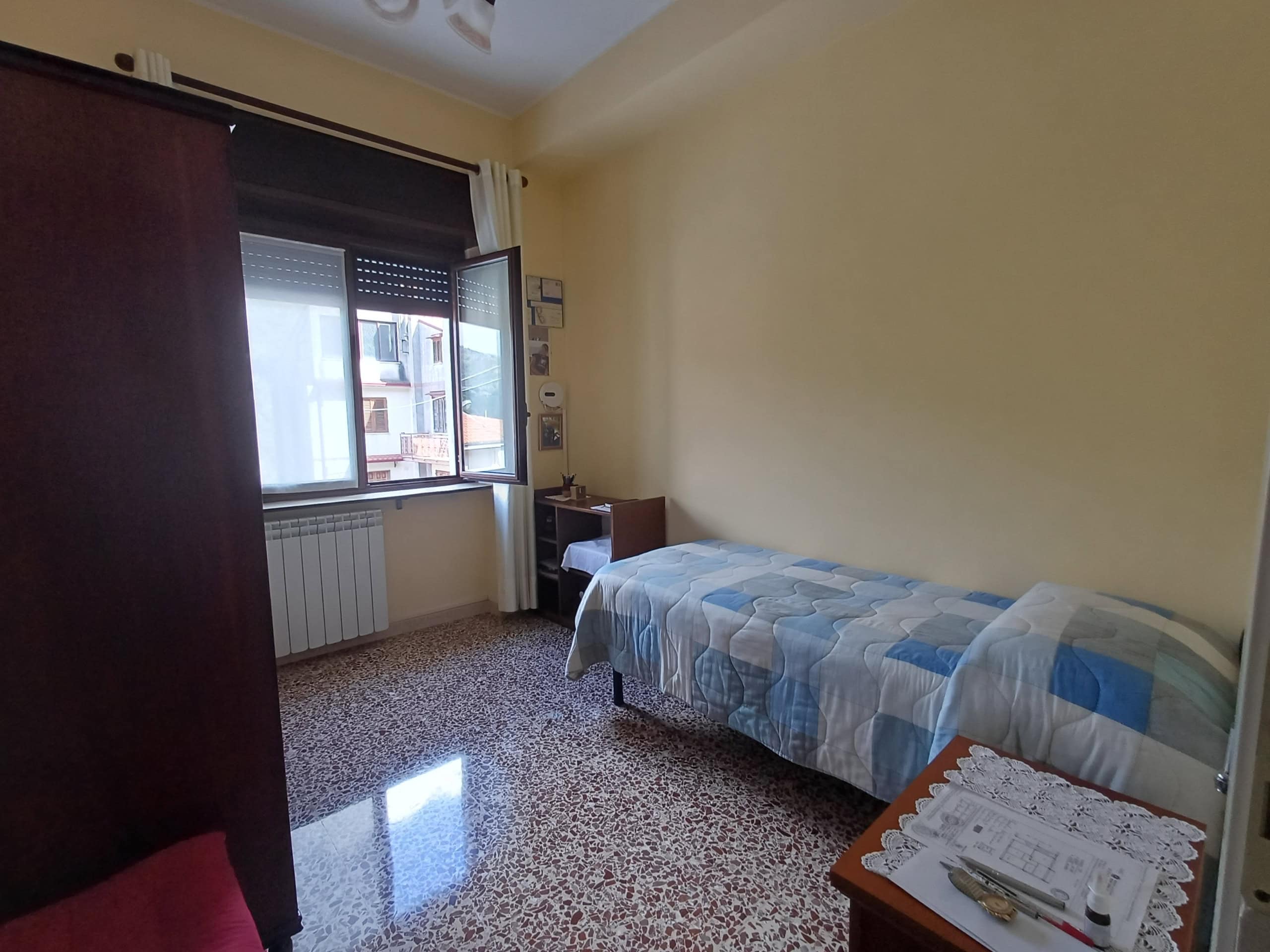 Letto singolo in camera da letto con finestra luminosa e arredamento semplice, ideale per affitti a breve termine o studenti. Spazio accogliente e funzionale con vista sulla città.
