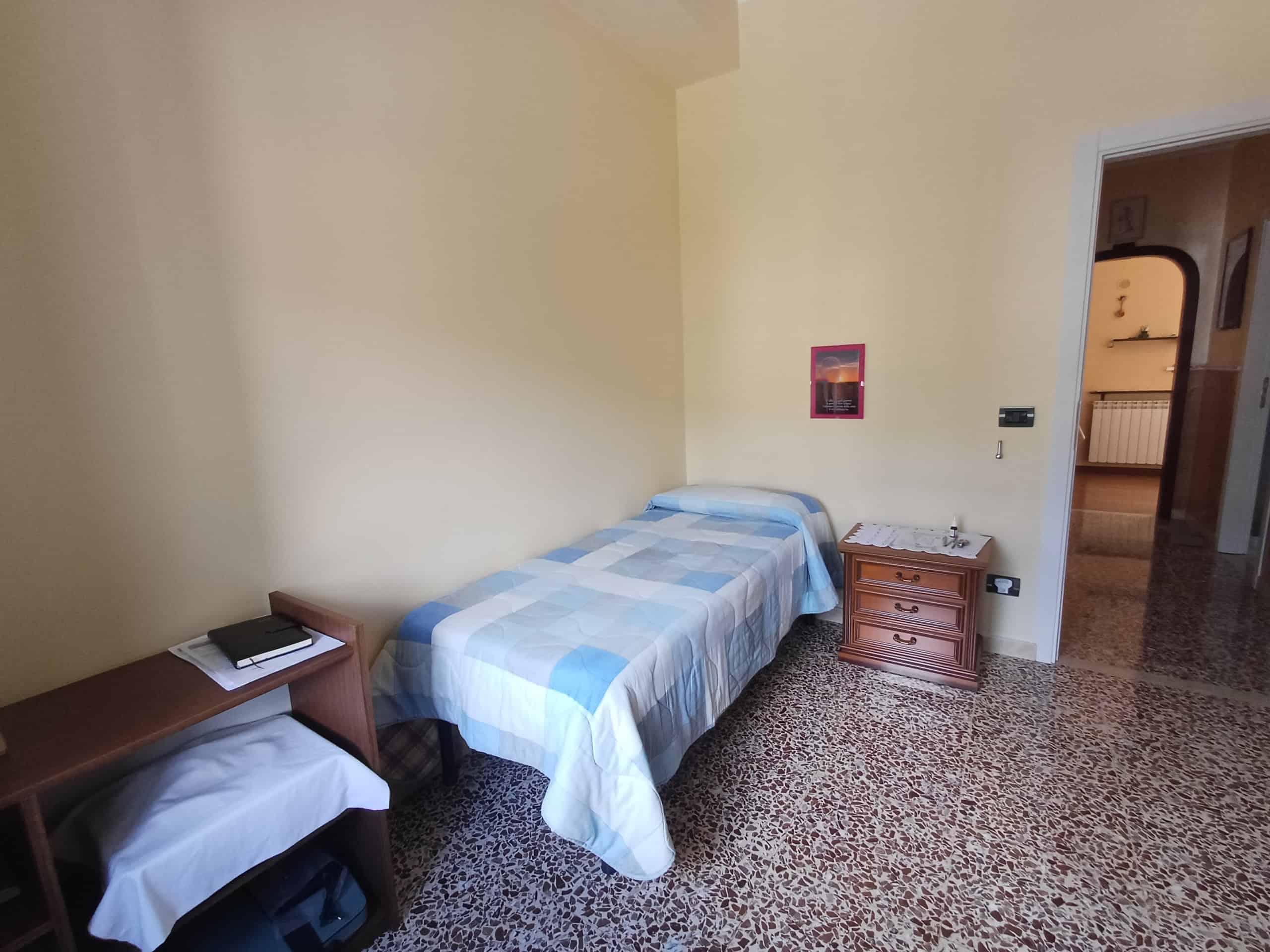 Camera da letto singola con letto singolo, comodino e armadio in una casa moderna, pavimento in marmo, pareti beige, ambiente luminoso e accogliente, ideale per affitti brevi o residenziali.