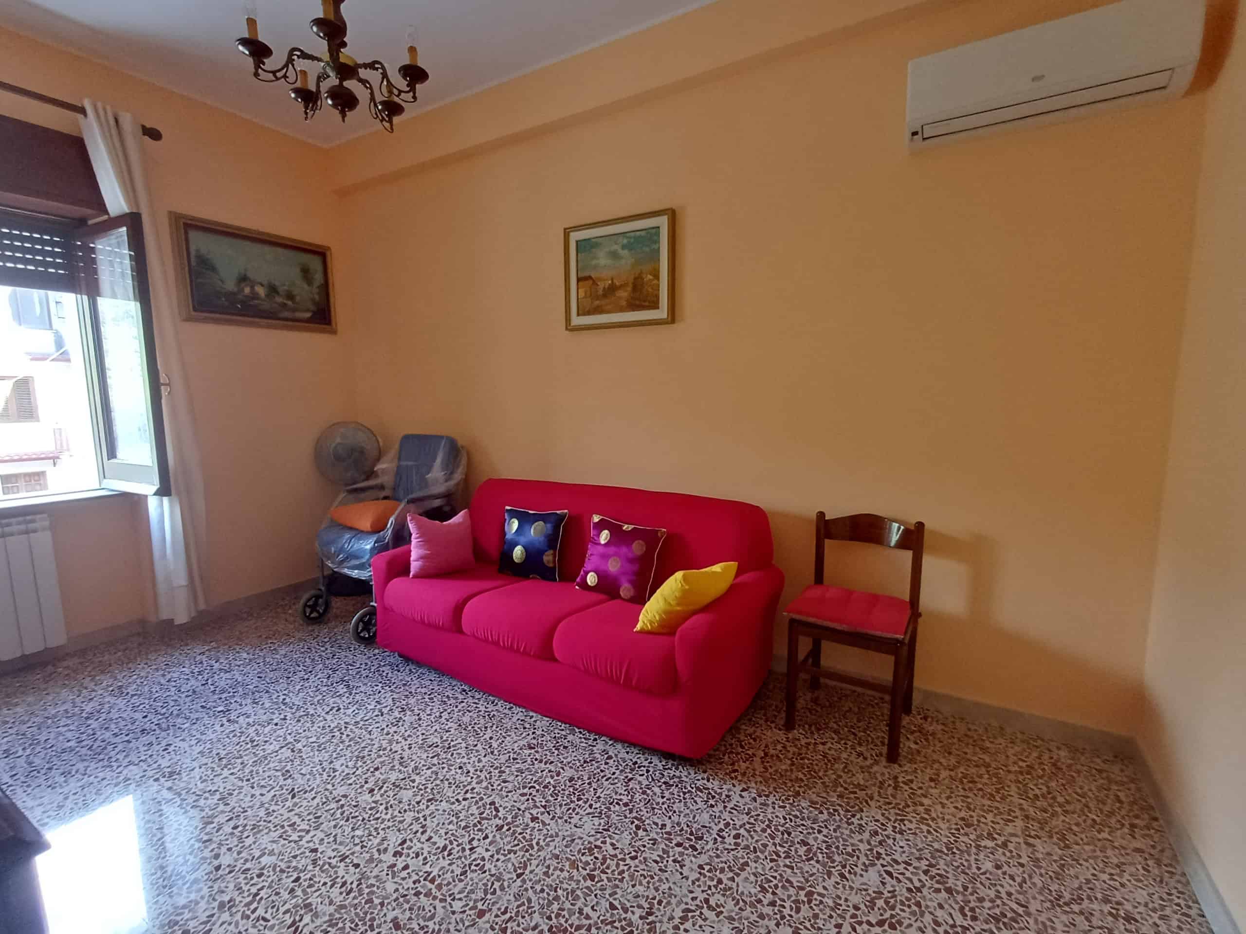 Soggiorno accogliente con divano rosa, quadri alle pareti e aria condizionata, ideale per relax e incontri familiari in appartamento a NextCasa.
