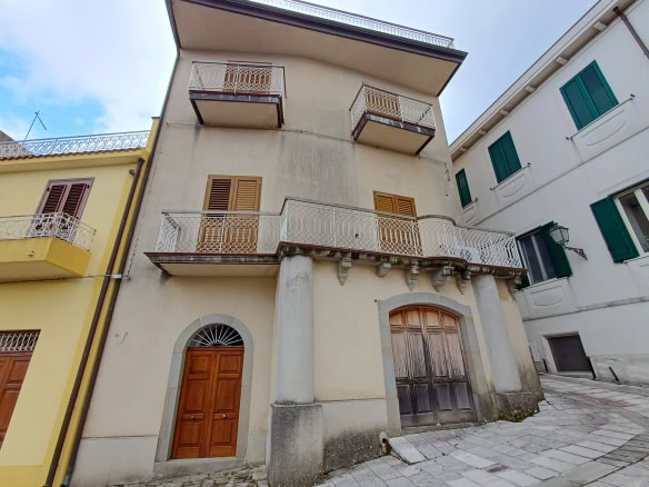 Balcone e facciata di un edificio storico in stile mediterraneo con dettagli in pietra e legno, situato in un quartiere pittoresco e caratteristico.