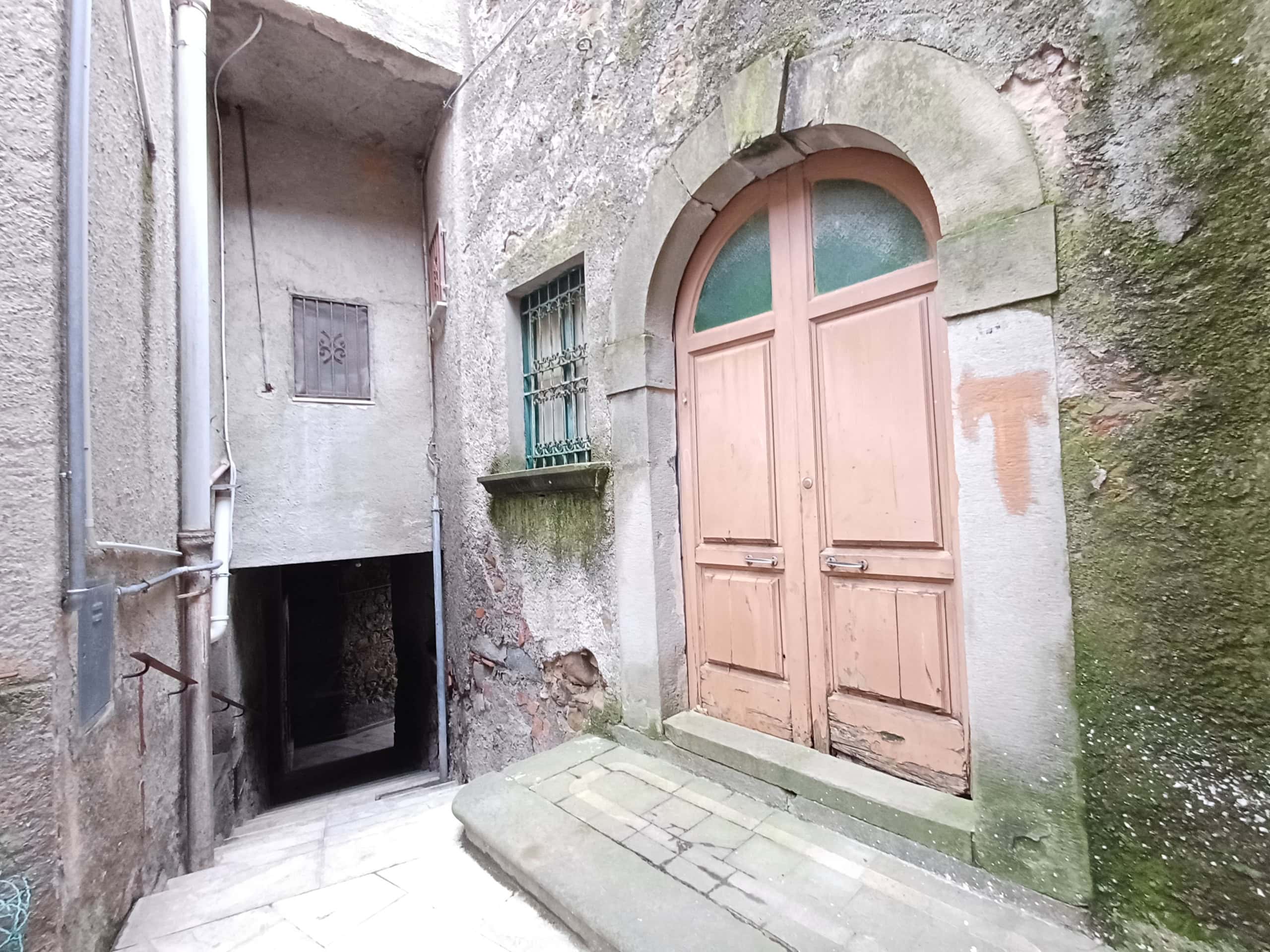 Antico portone in legno con arco in pietra, ingresso di un edificio storico in un vicolo di città.
