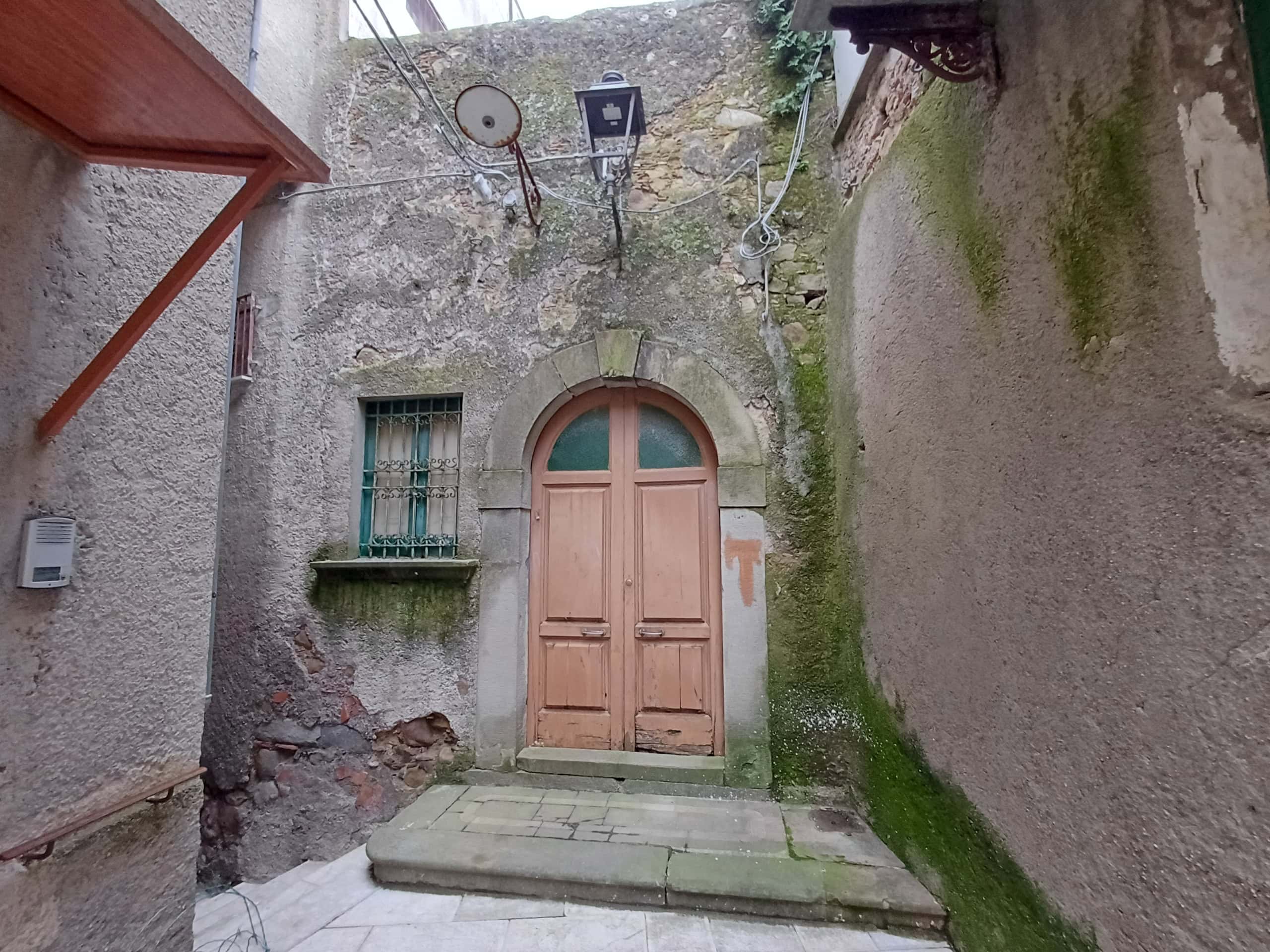 Vecchio portone in legno con pareti di pietra e muschio, ingresso in un cortile storico italiano, atmosfera rustica e autentica, ideale per case di charme o ristrutturazioni tradizionali.