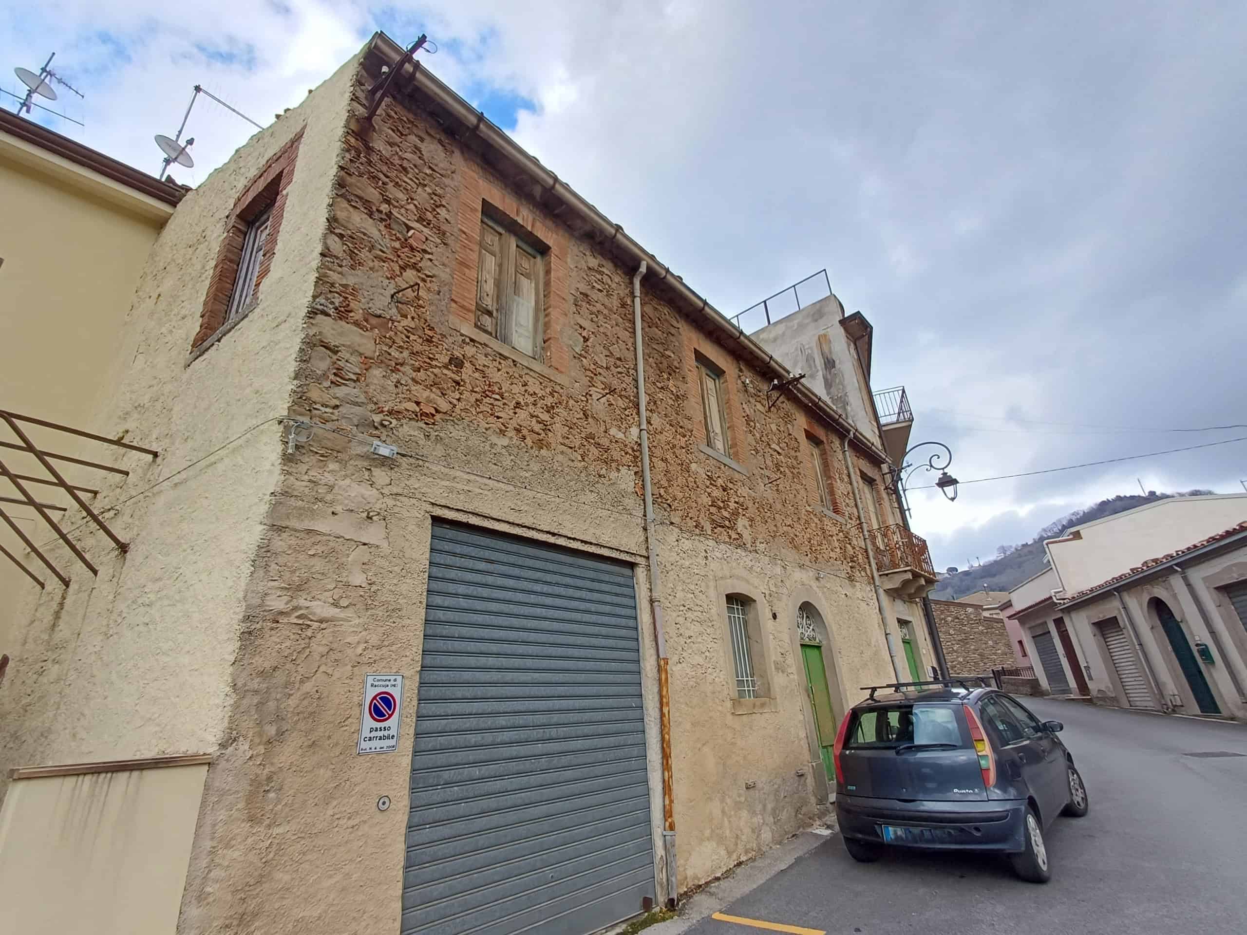 Edificio storico in pietra con garage e strada di paese, situato in zona tranquilla e panoramica, ideale per investimento immobiliare o ristrutturazione.